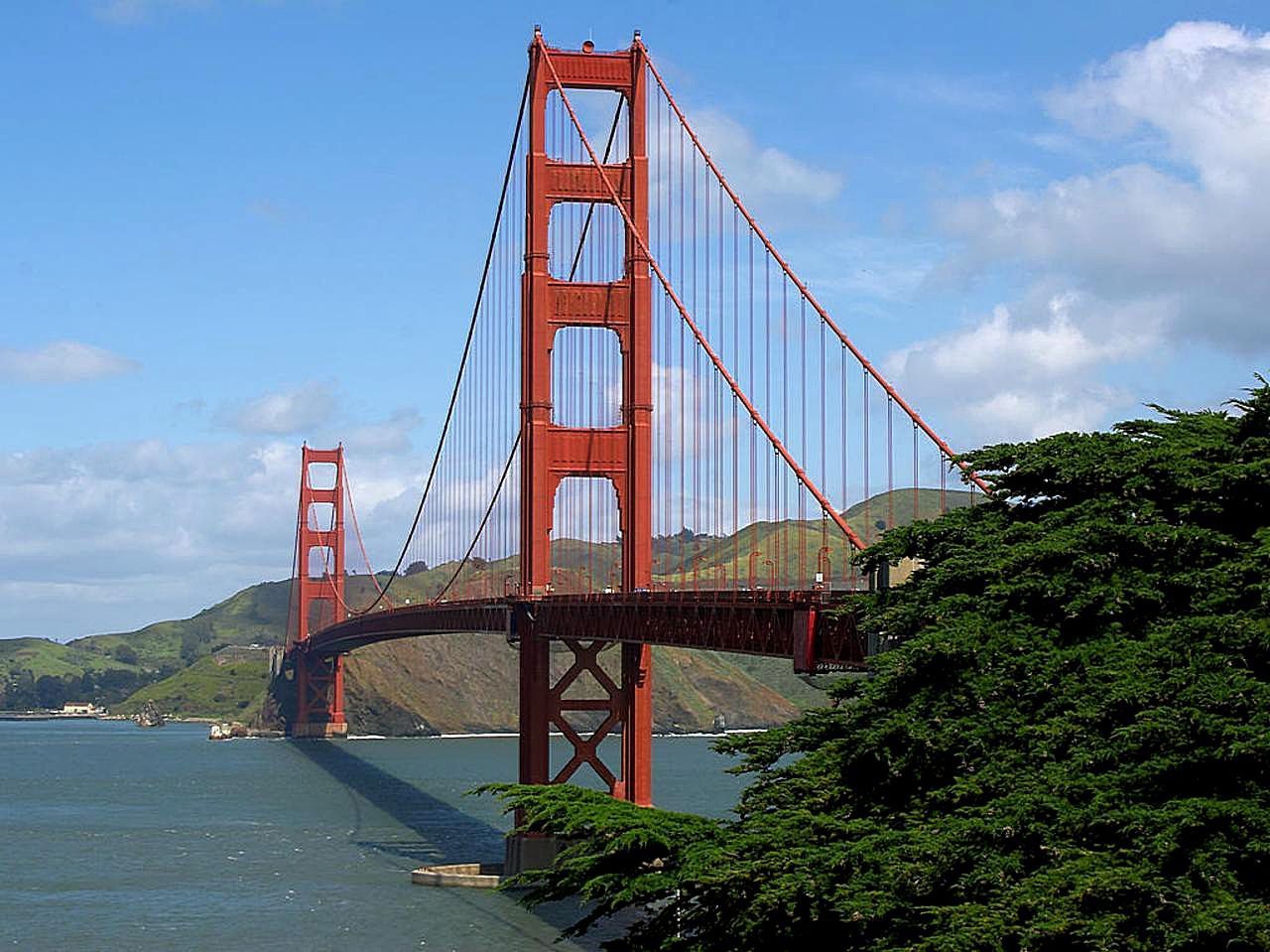 Red suspension bridge over water, green hills, and partly cloudy sky. - Bay Area Ridge Trail: Golden Gate Bridge