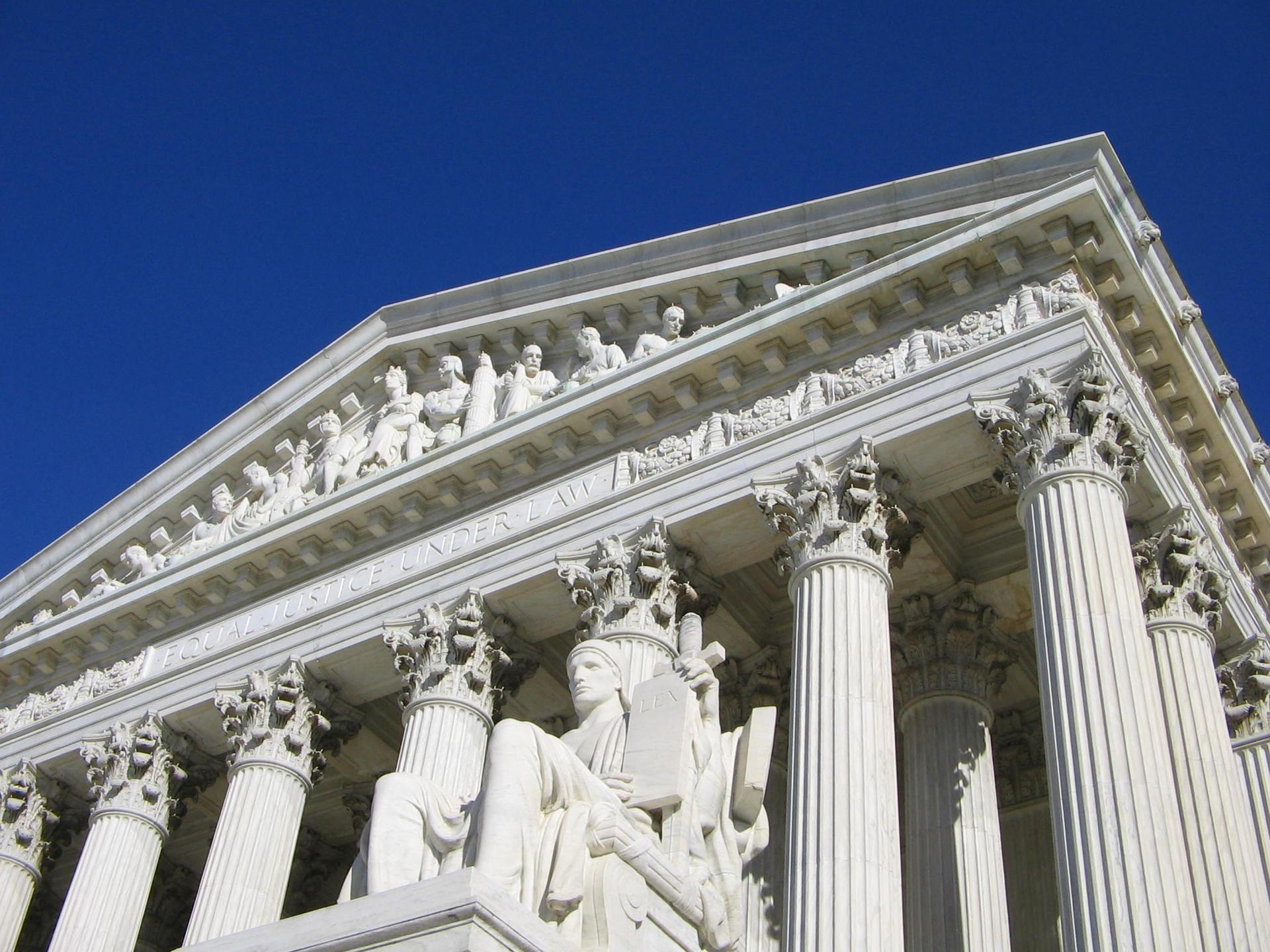 Close-up of ornate white stone building with statues under a blue sky.