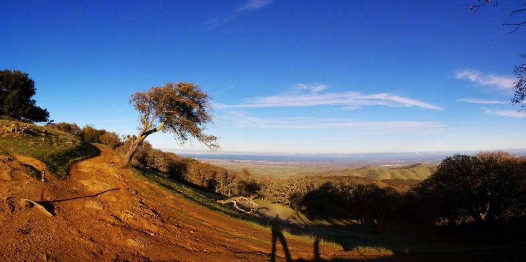 A winding dirt path on a sunlit hillside overlooking a vast valley.