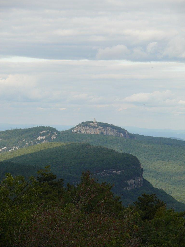 Distant mountain peak with a building on top, surrounded by green forests.