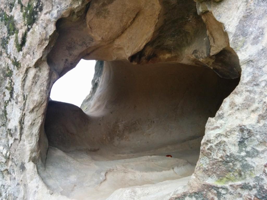 Close-up of a dark, natural cave opening in light-colored rock.