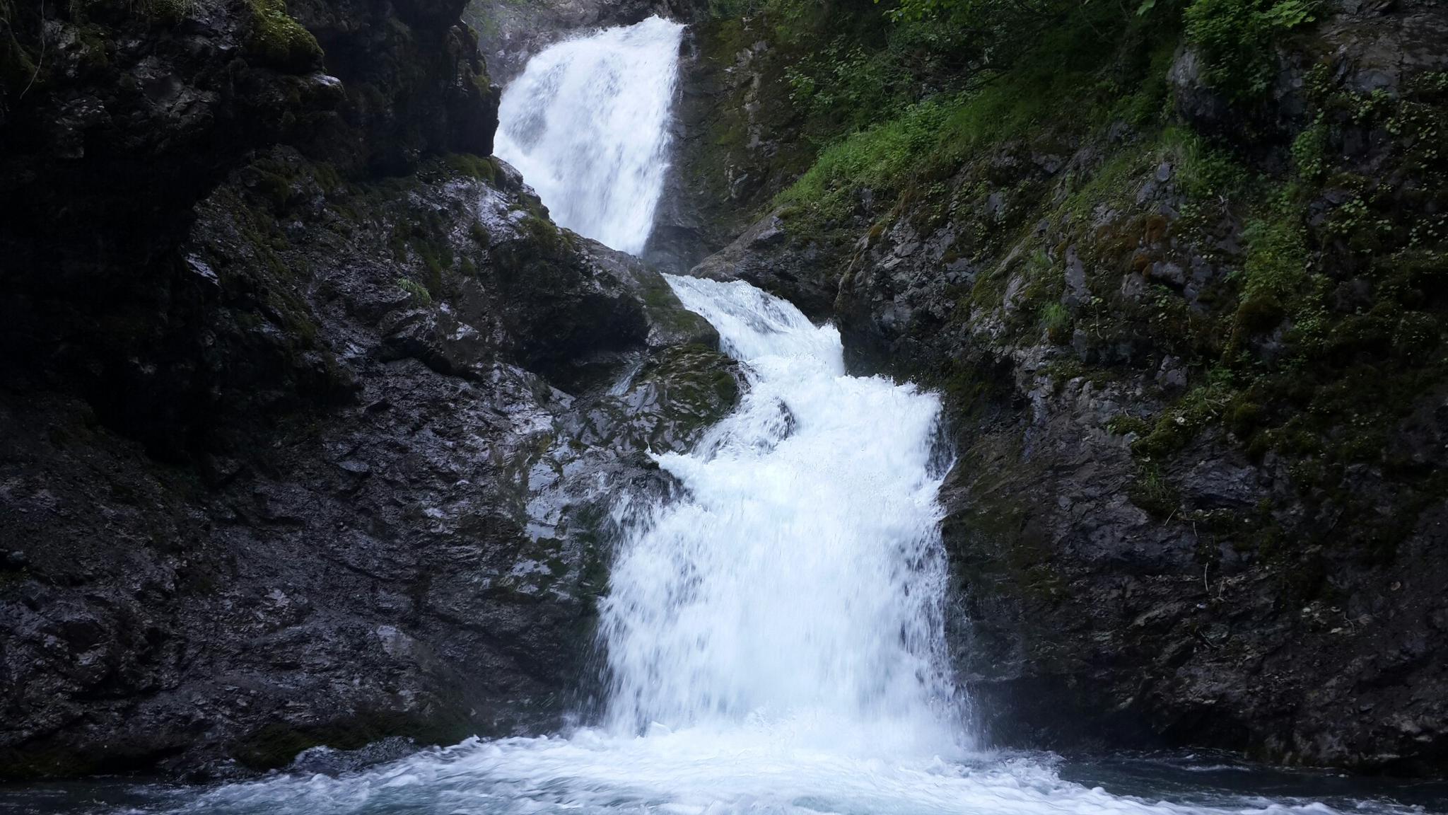 Powerful waterfall cascades over dark, mossy rocks into a pool below.