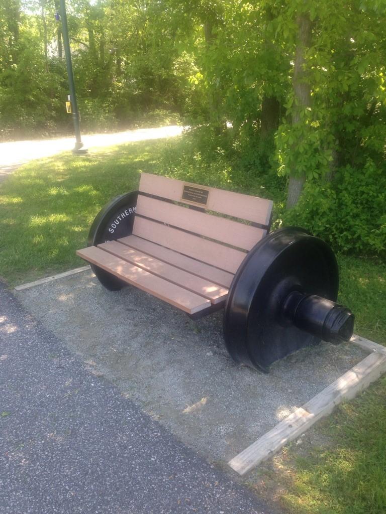 Unique park bench with train wheel sides in a grassy, sunny area.