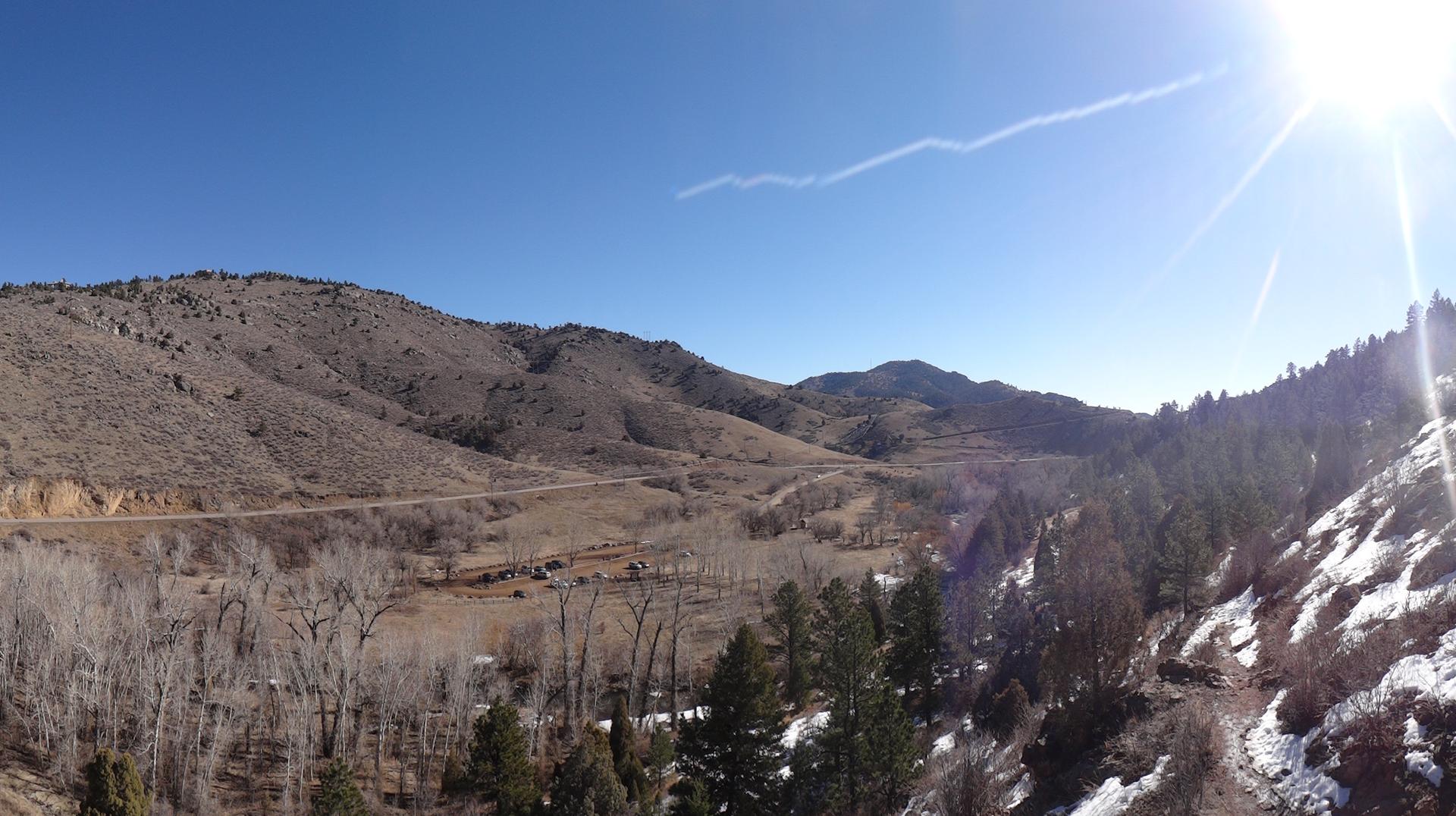 Wide mountain landscape with valleys, snow, bare trees, and bright sun.