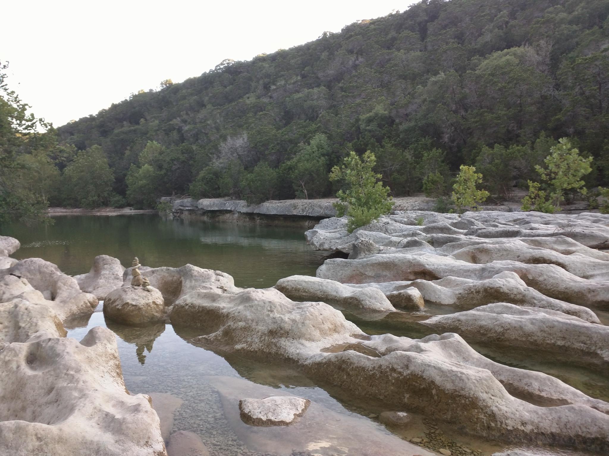 Calm river flowing through rocky terrain with forested hills in the background.