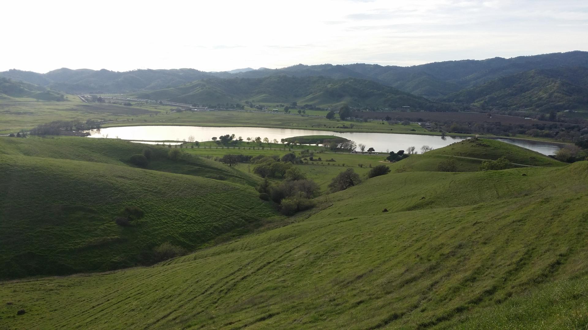 A serene lake nestled among rolling green hills under an overcast sky.