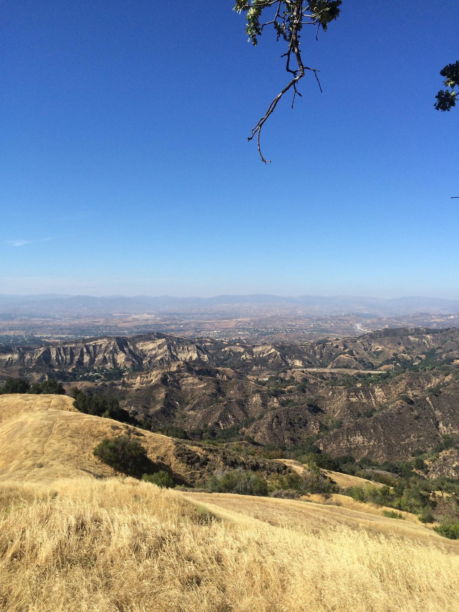Expansive view of dry, rolling hills and distant mountains under a clear sky.