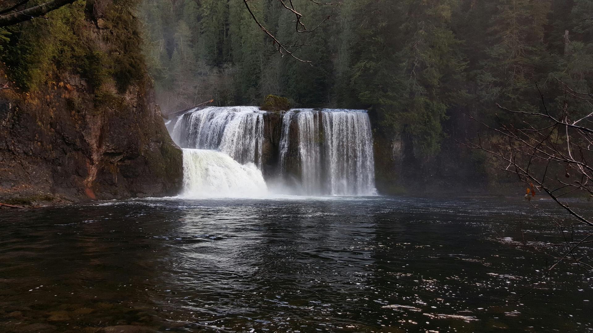 Powerful waterfall plunging into a dark river, surrounded by dense forest.