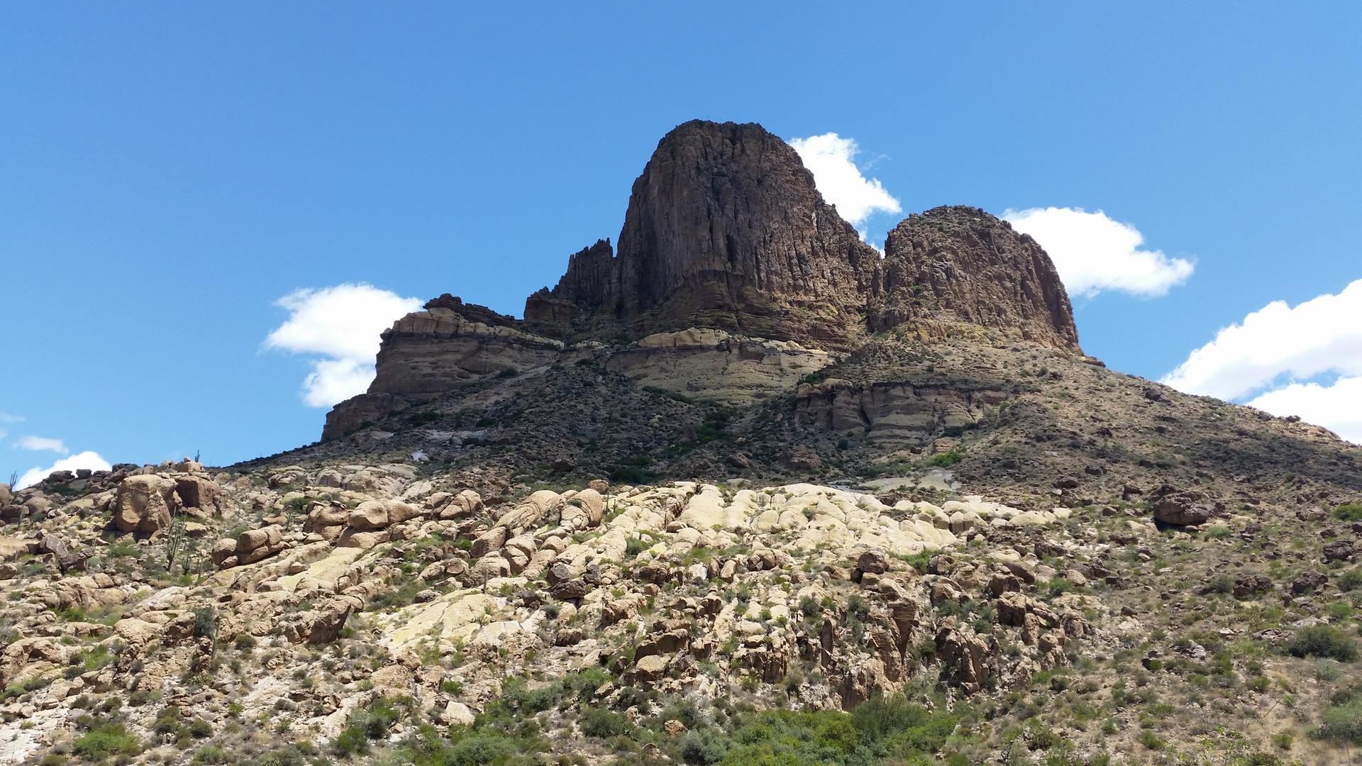 Large, rounded rock formations dominate a desert landscape under a blue sky.