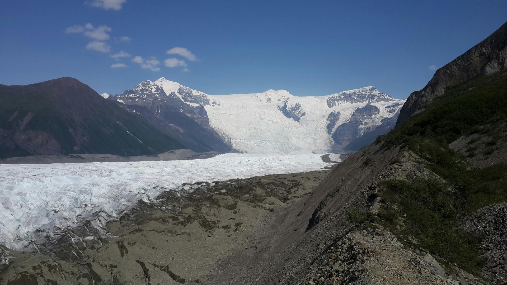 A massive glacier filling a valley, surrounded by mountains on a clear day.