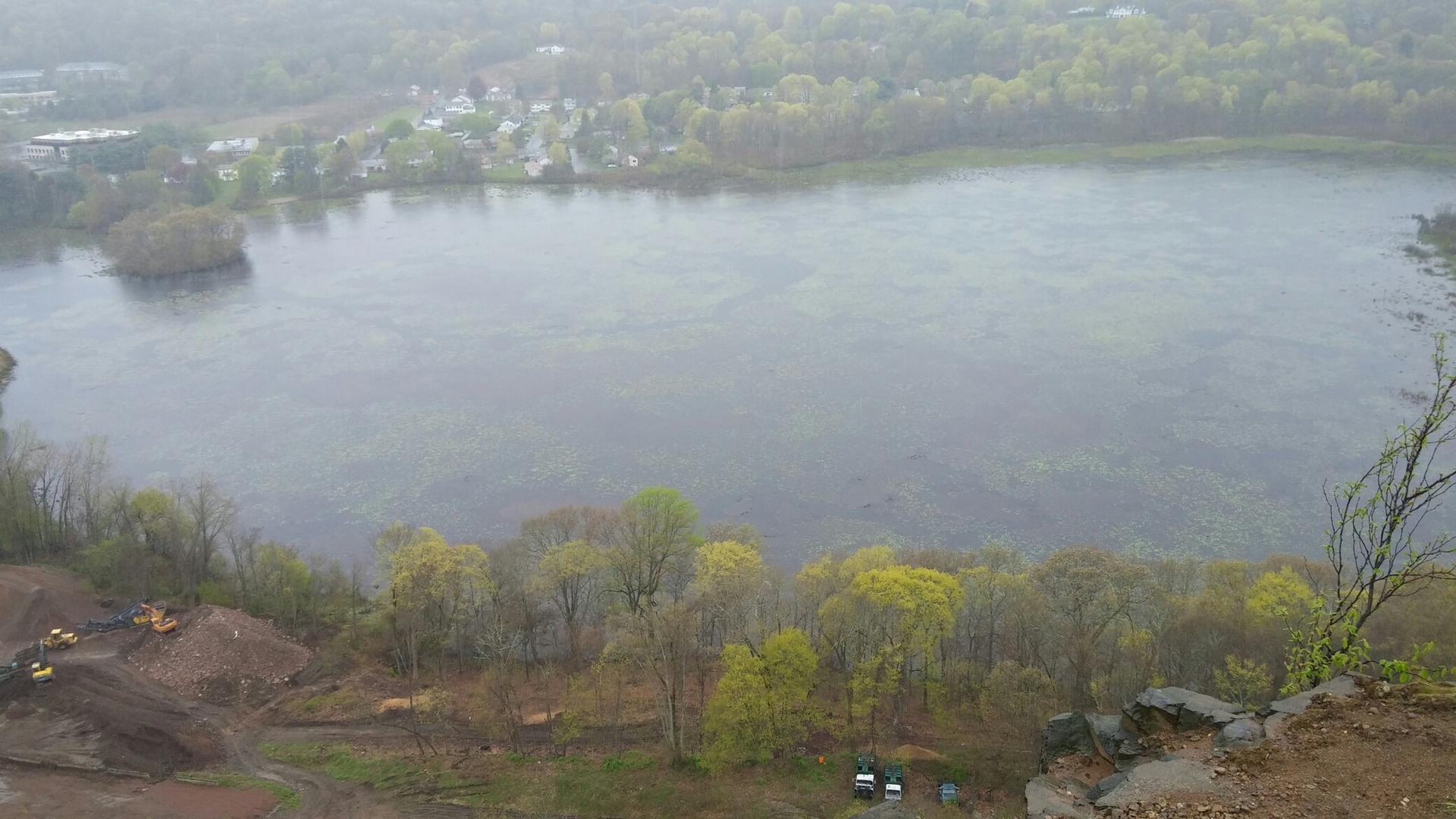 Overlook of a large lake, green forests, and construction under an overcast sky.