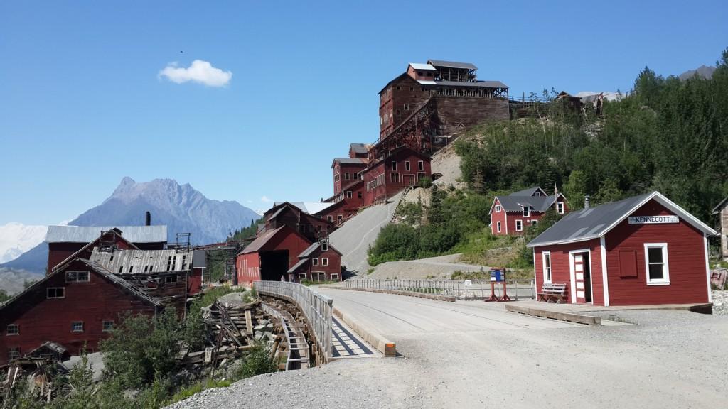 Red historical buildings on a sunny hillside with mountains in background.