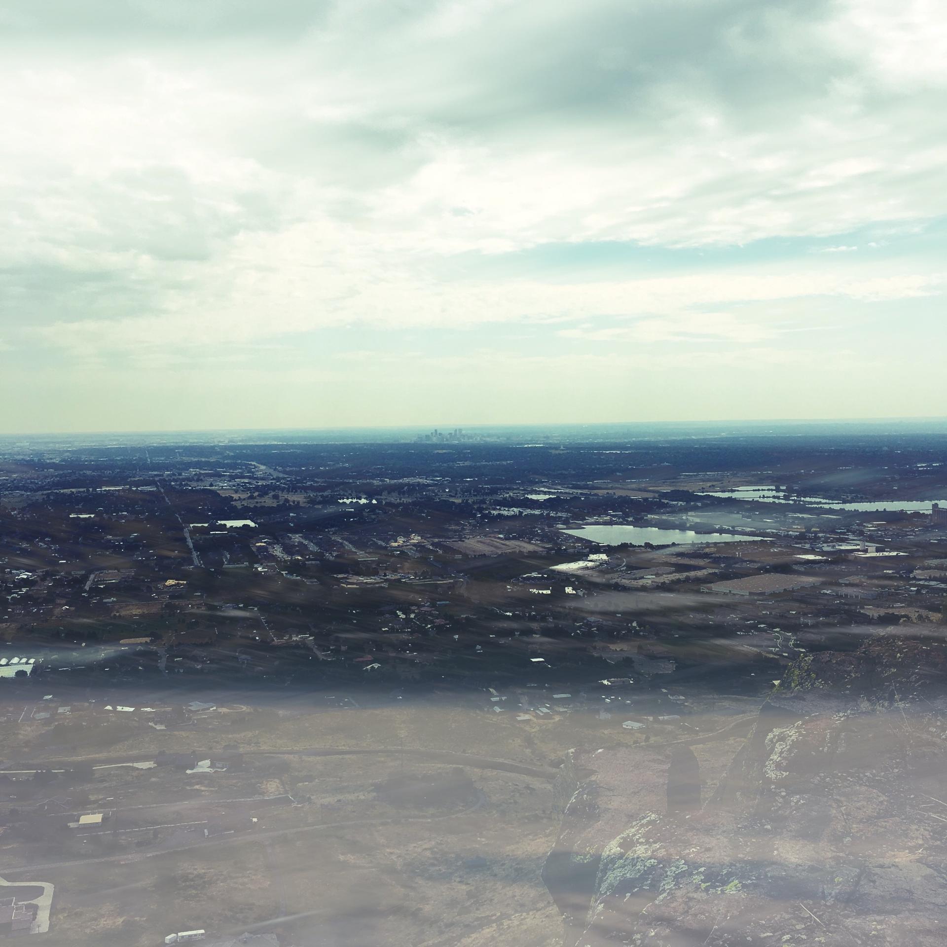 An aerial view shows a vast, hazy landscape with cities and water.