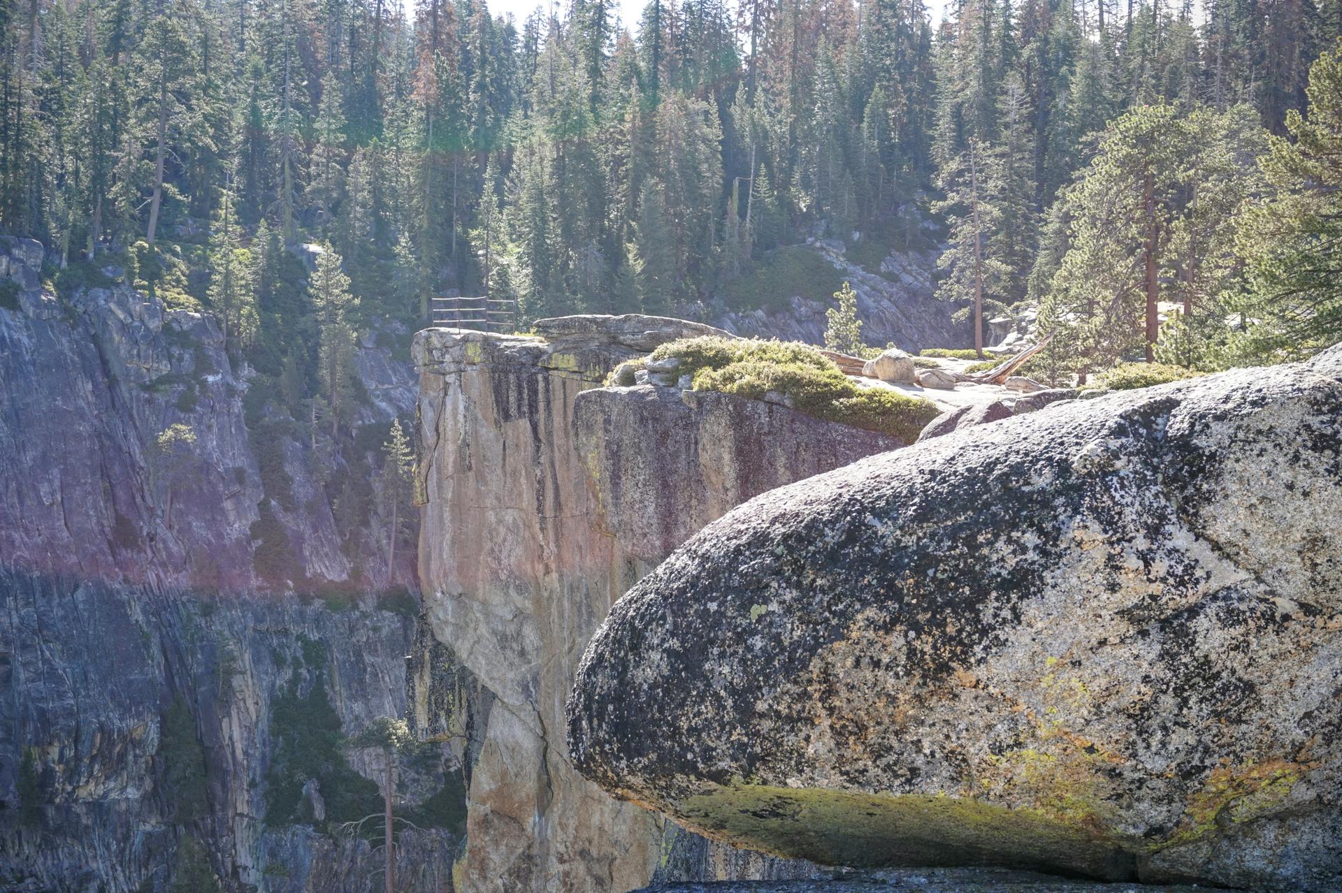 A large boulder on a cliff edge overlooking a deep forested canyon.