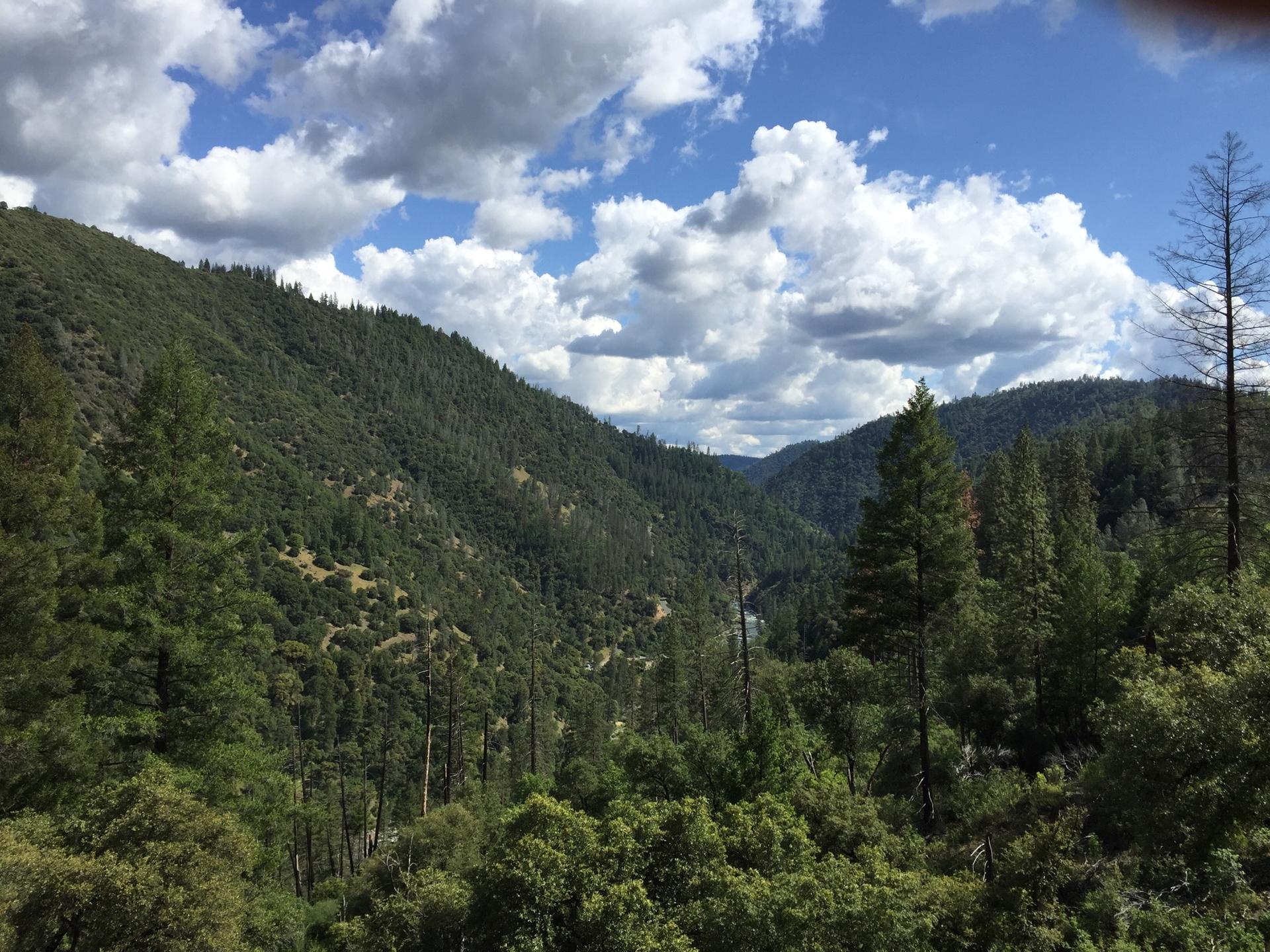 Dense green forests cover steep mountains under a bright, cloudy sky.