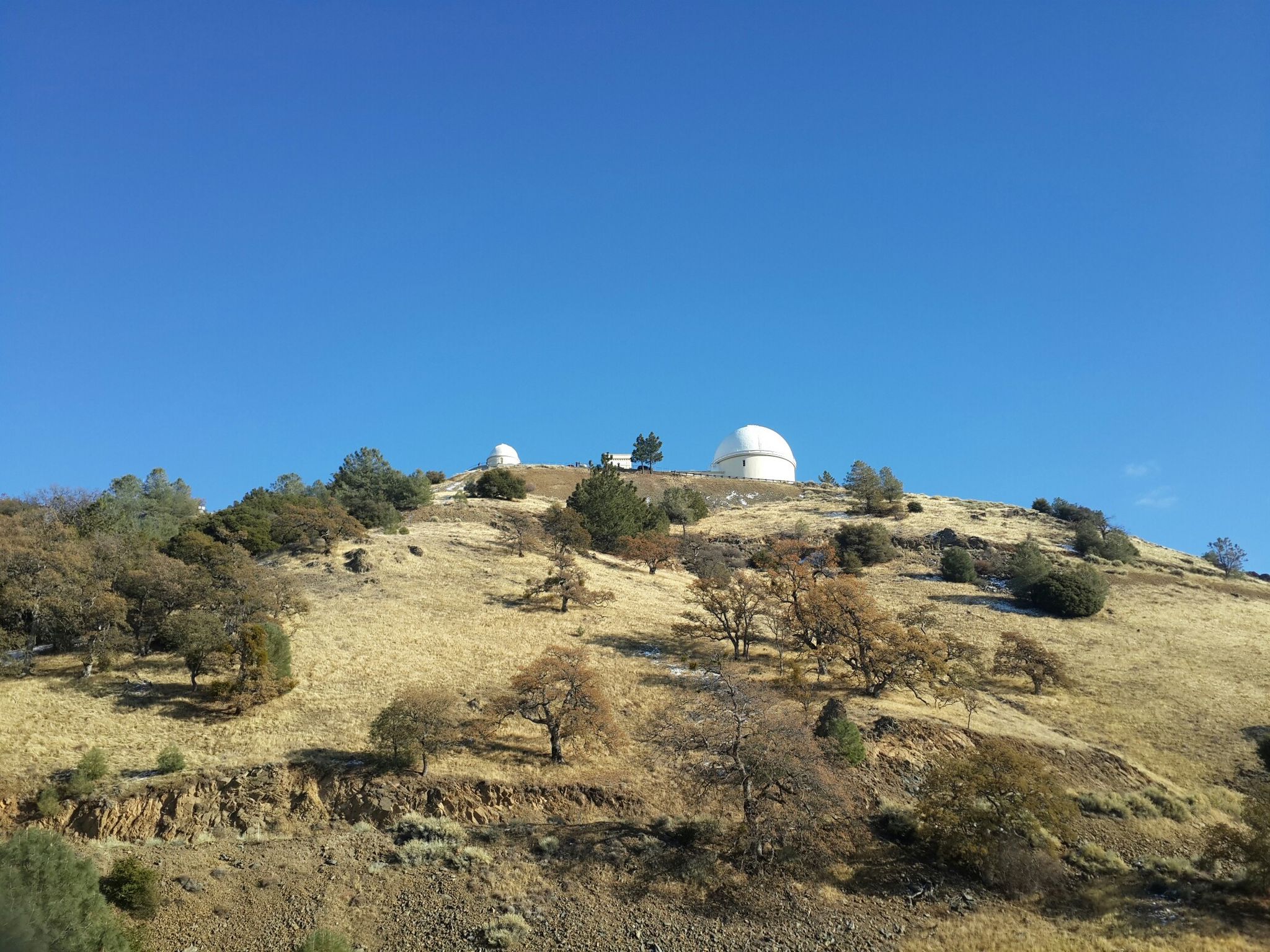 White observatory domes on a dry, tree-covered hill under a blue sky. - Mount Hamilton & JD Grant Park loop from Berryessa
