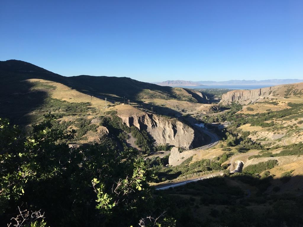 Sunny valley view with a winding road, river, and distant water.