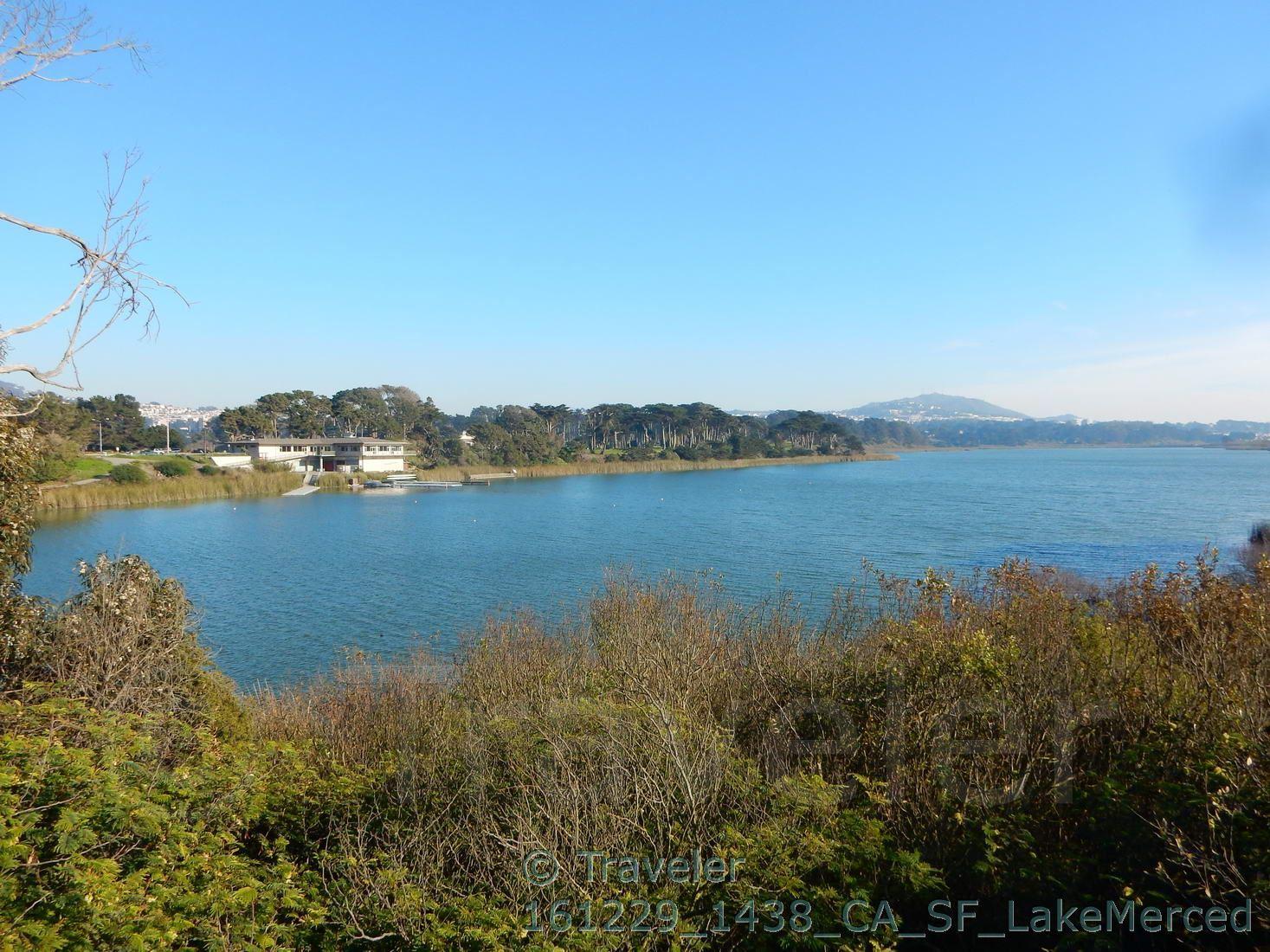 A wide lake surrounded by green trees and distant buildings under a clear sky.