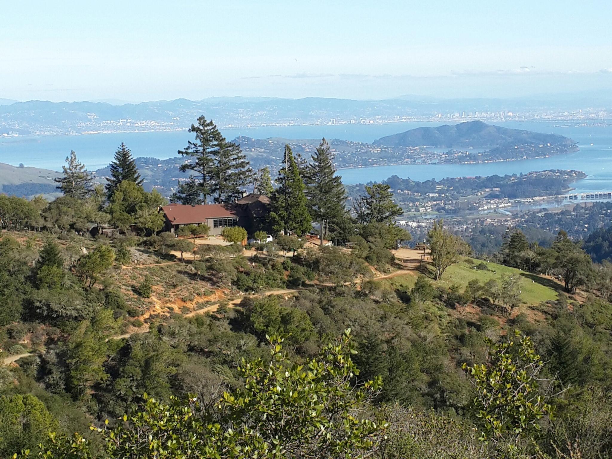 House on a green hill overlooking a bay and distant city.