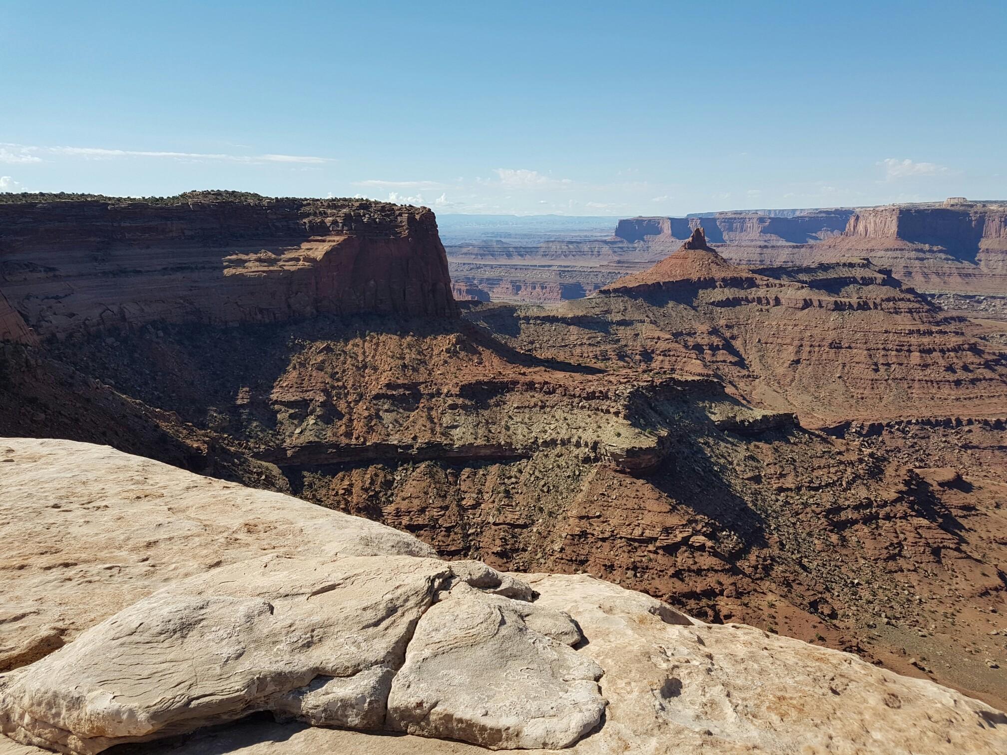 Rocky foreground overlooking a vast, layered canyon under a clear sky.