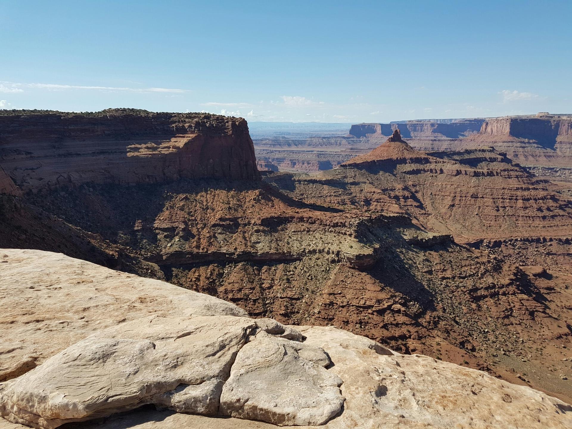 Rocky foreground overlooking a vast, layered canyon under a clear sky.