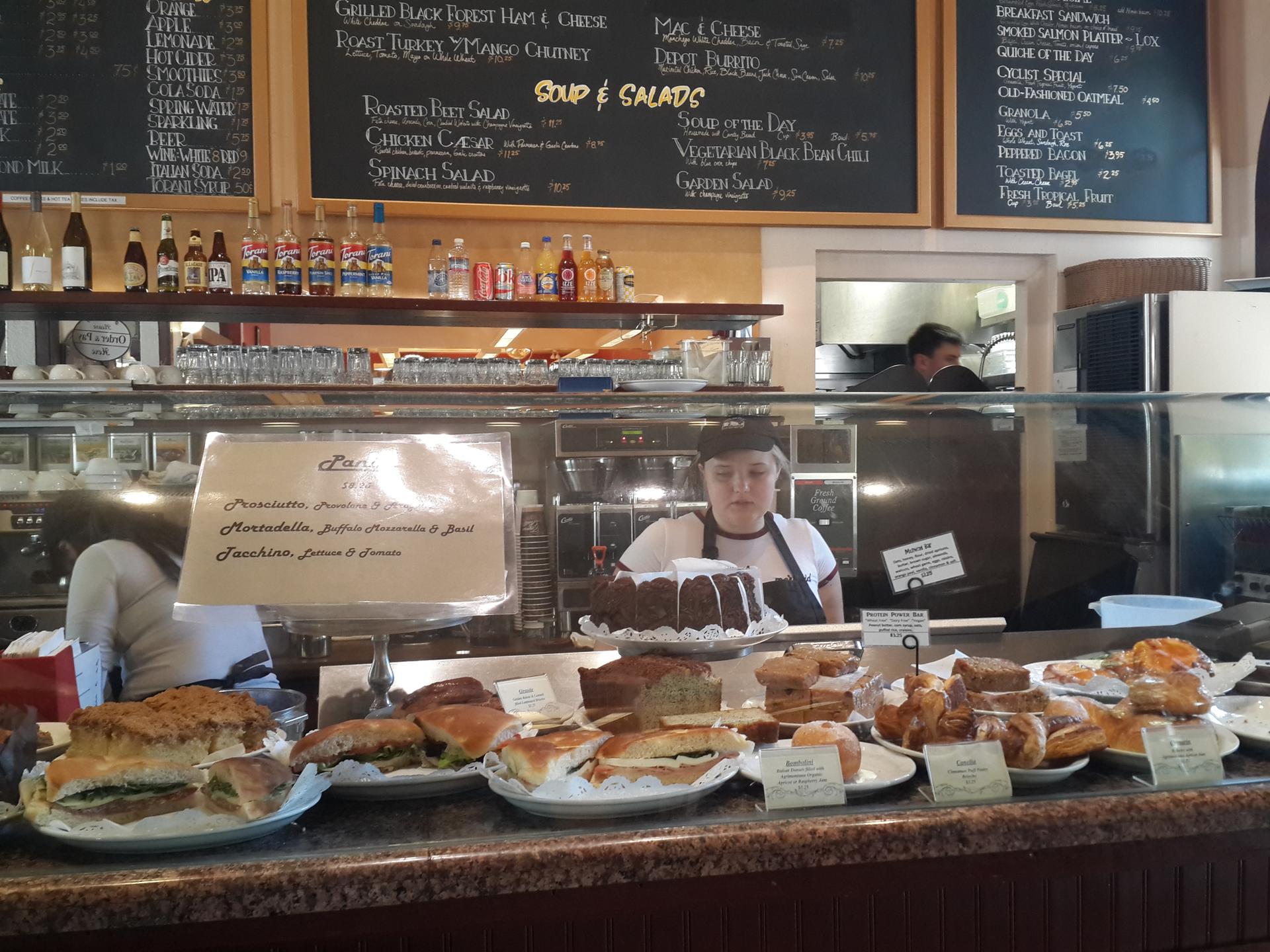 A bakery counter filled with pastries and sandwiches, with staff working.