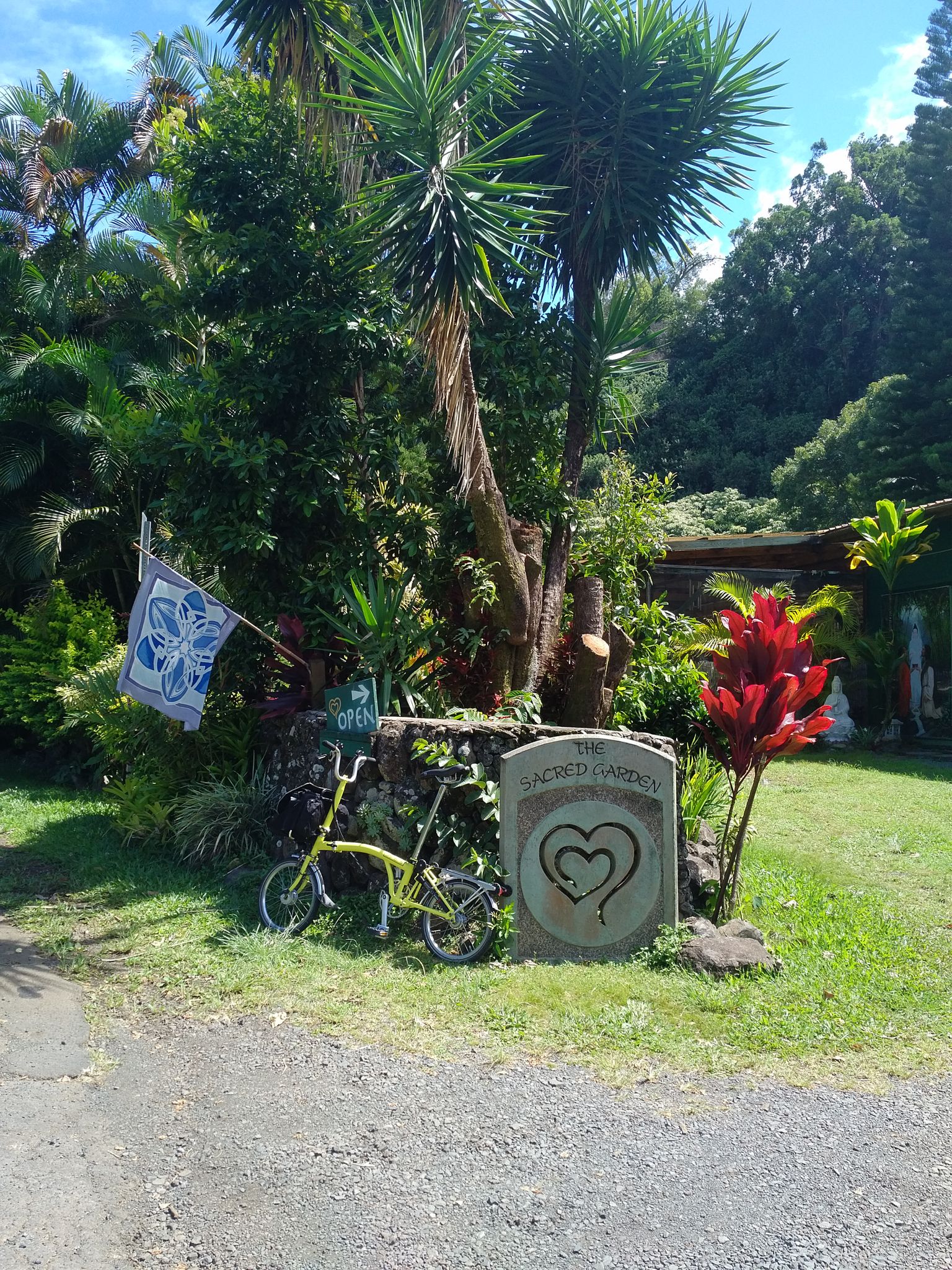 A yellow bicycle parked next to a stone sign amidst lush tropical plants. - Kokomo Road via West Kuiaha Road loop
