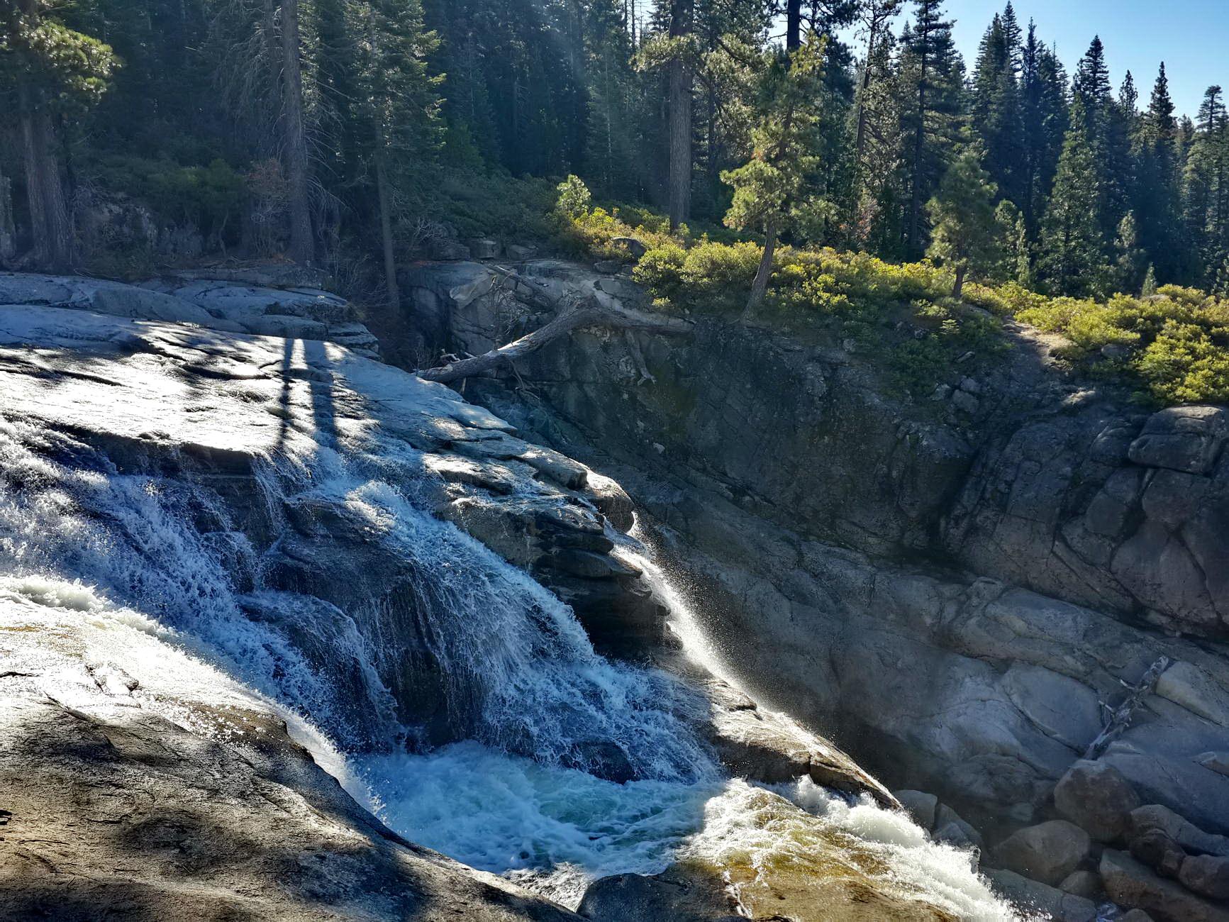 Sunlit waterfall cascades over granite rocks in a lush forest.