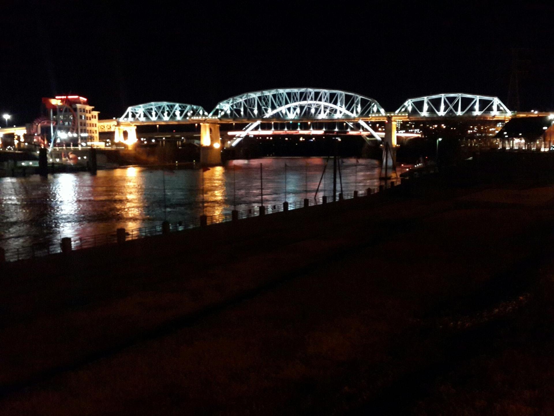 Brightly lit bridge over a dark river with city lights at night.