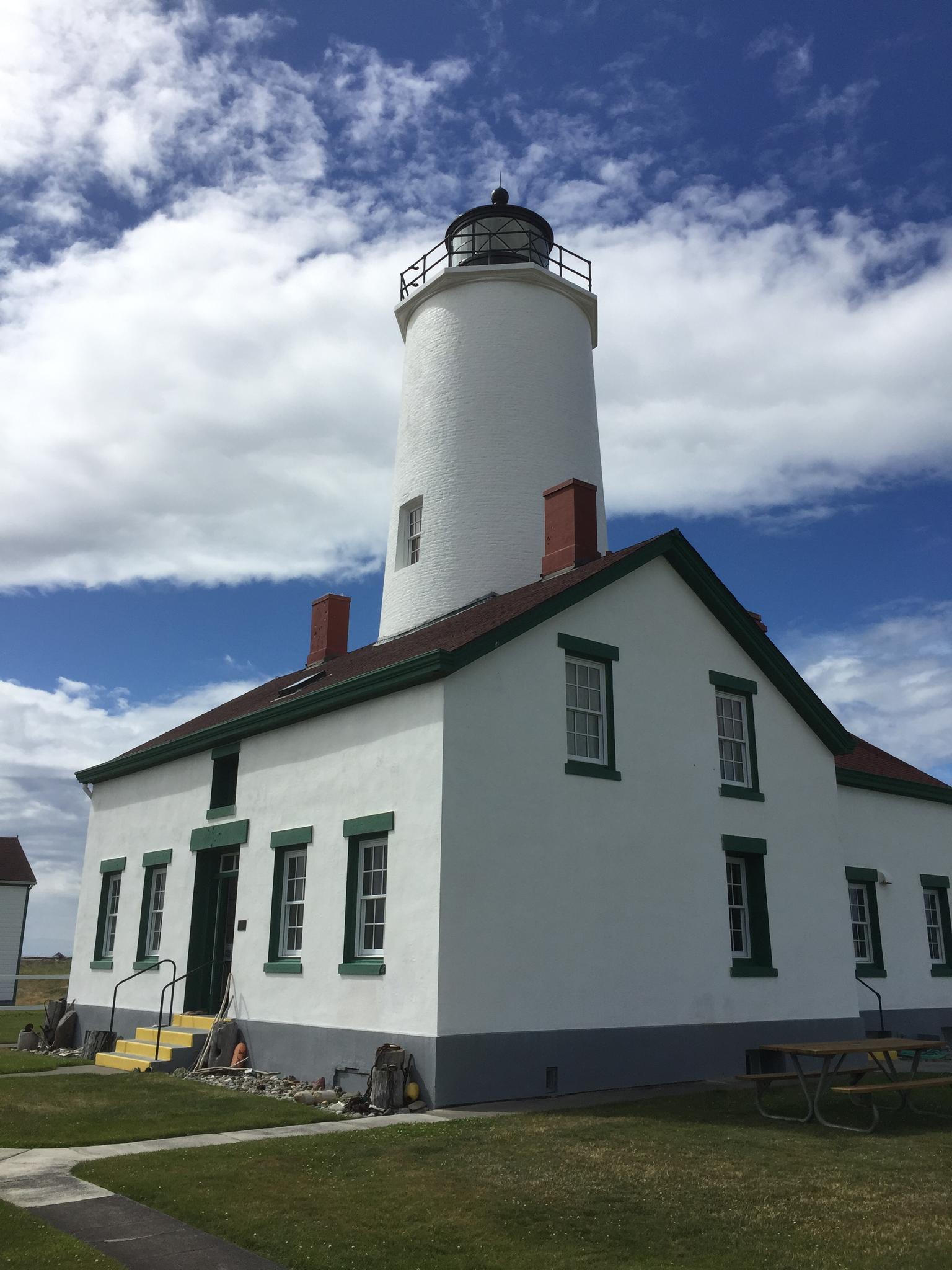A white lighthouse and keeper's house stand under a partly cloudy sky.