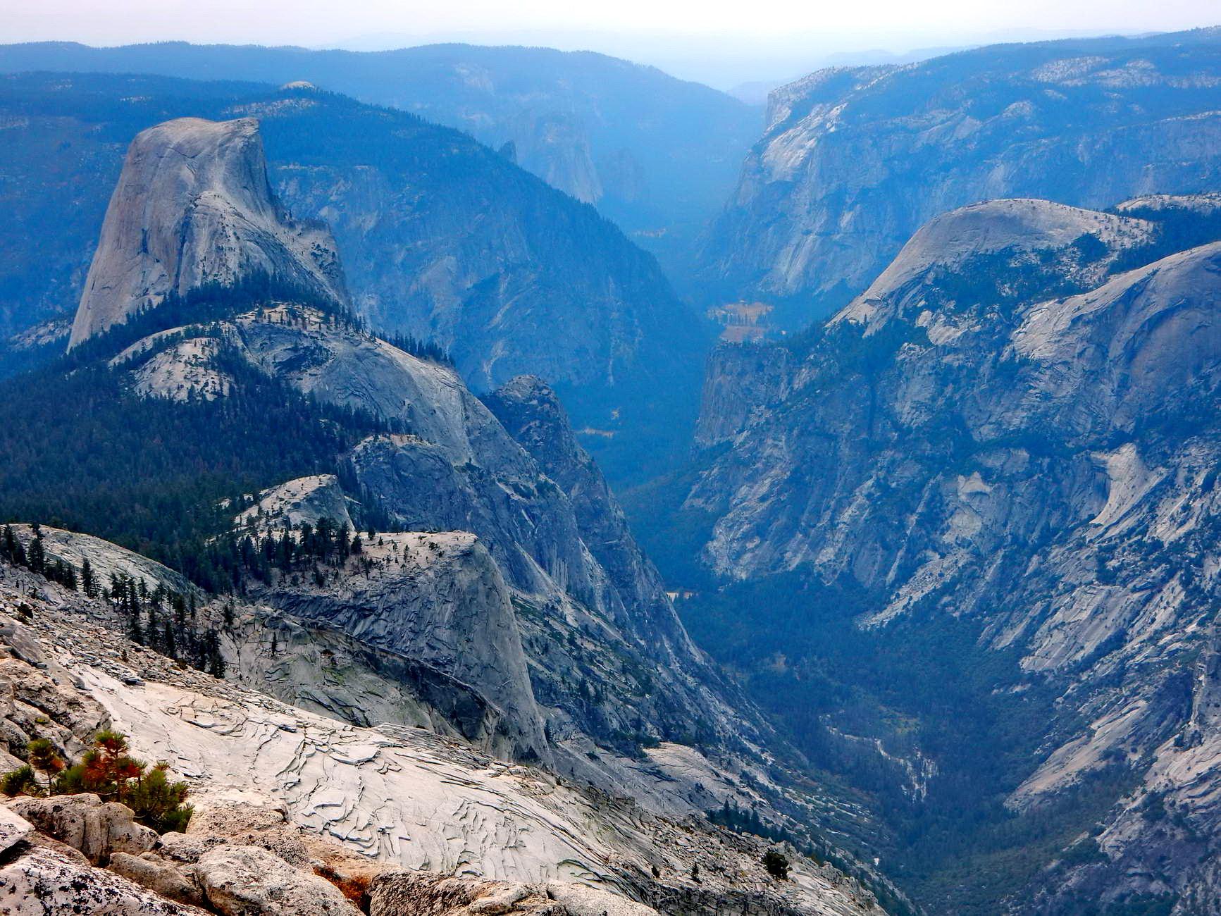 Vast mountain valley with prominent granite domes under a hazy sky.