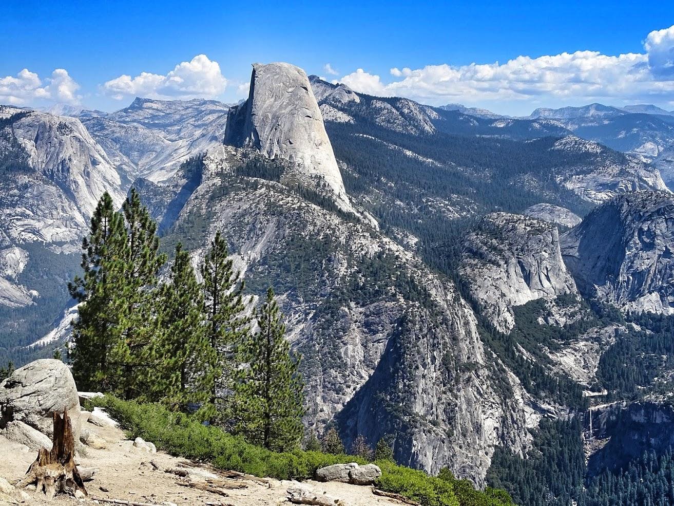 A massive granite dome rises above a vast, forested mountain range.
