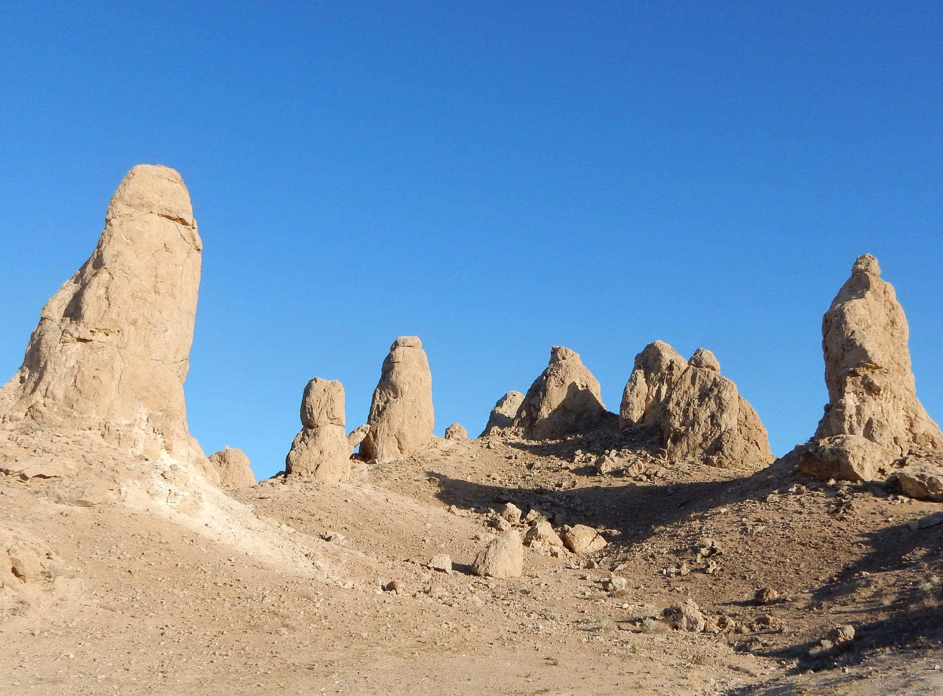 Tall, rugged rock formations rise from a desert floor under a clear blue sky.