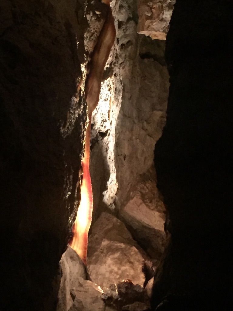 A glowing red cave formation illuminates a dark, narrow rocky passage. - Custer to Jewel Cave National Monument