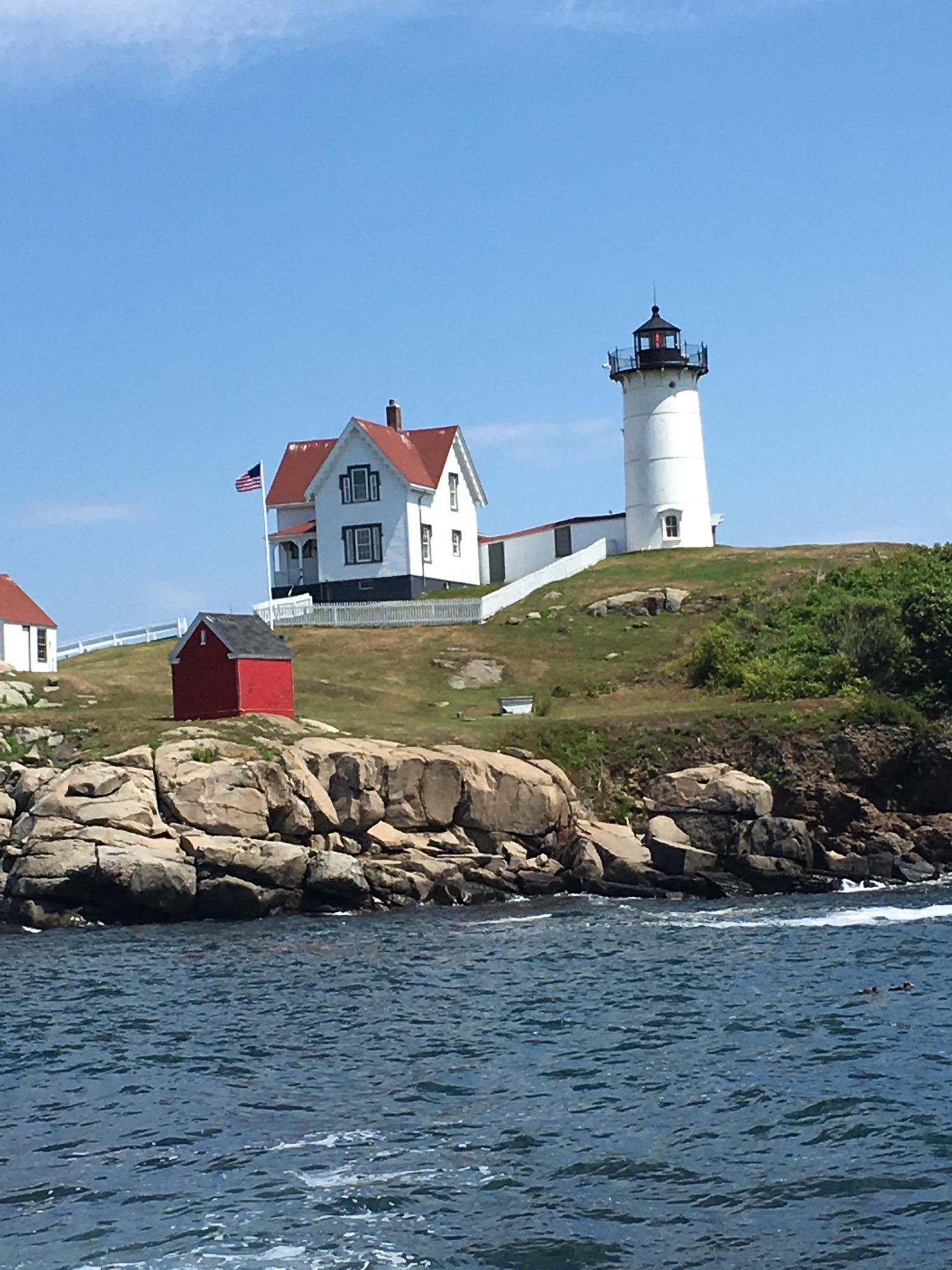 White lighthouse and house on a rocky island, bright sunny day.