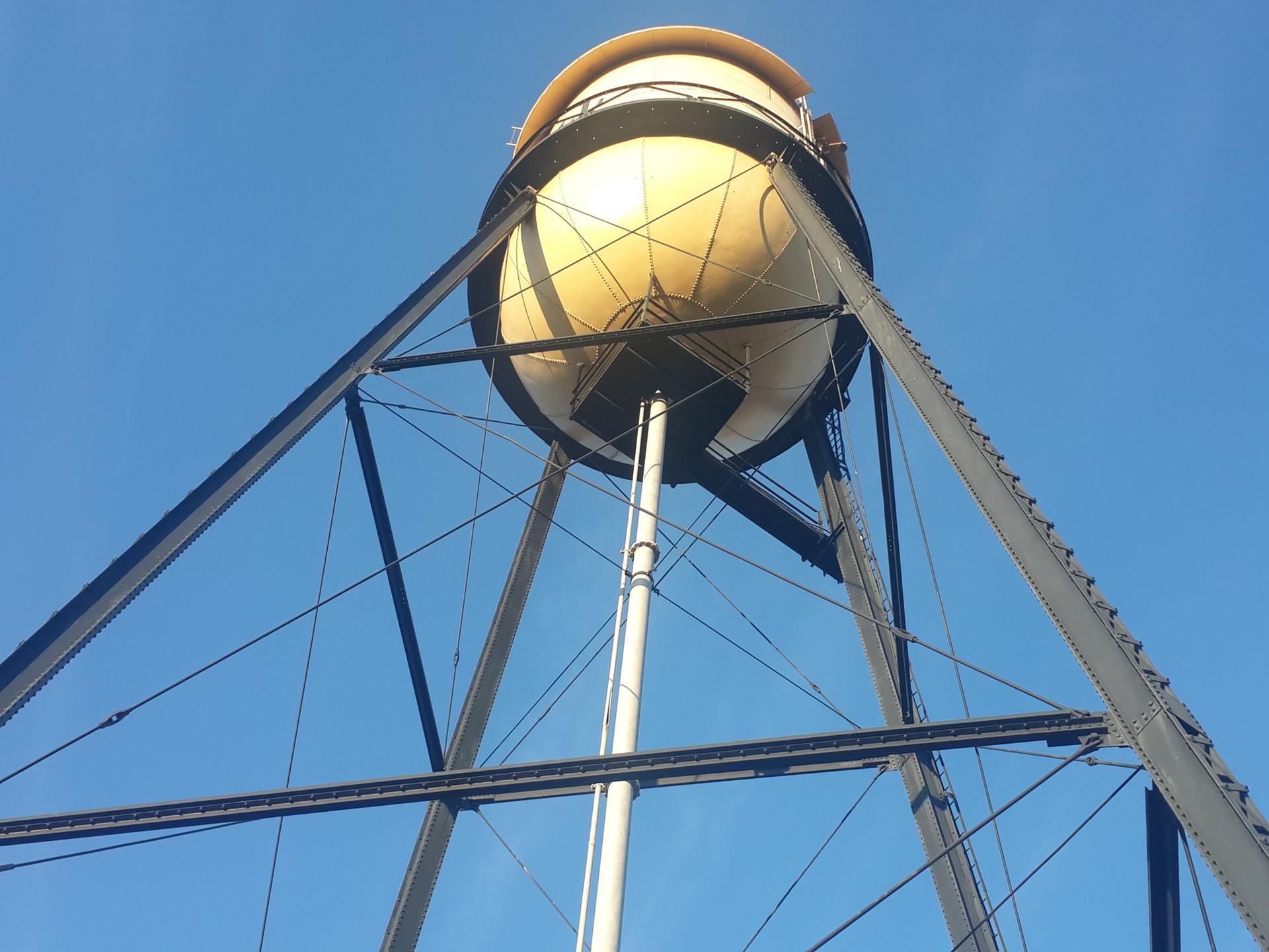 Low angle view of a large yellow water tower against a blue sky.