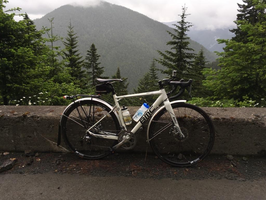 White bicycle parked on a concrete barrier with a cloudy mountain background.