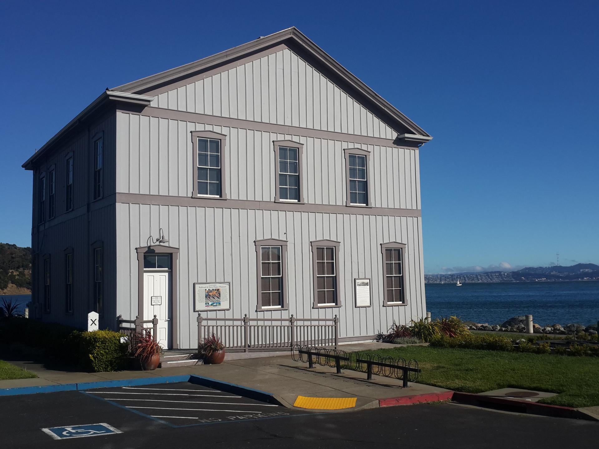 Gray two-story building by the water on a clear, sunny day.