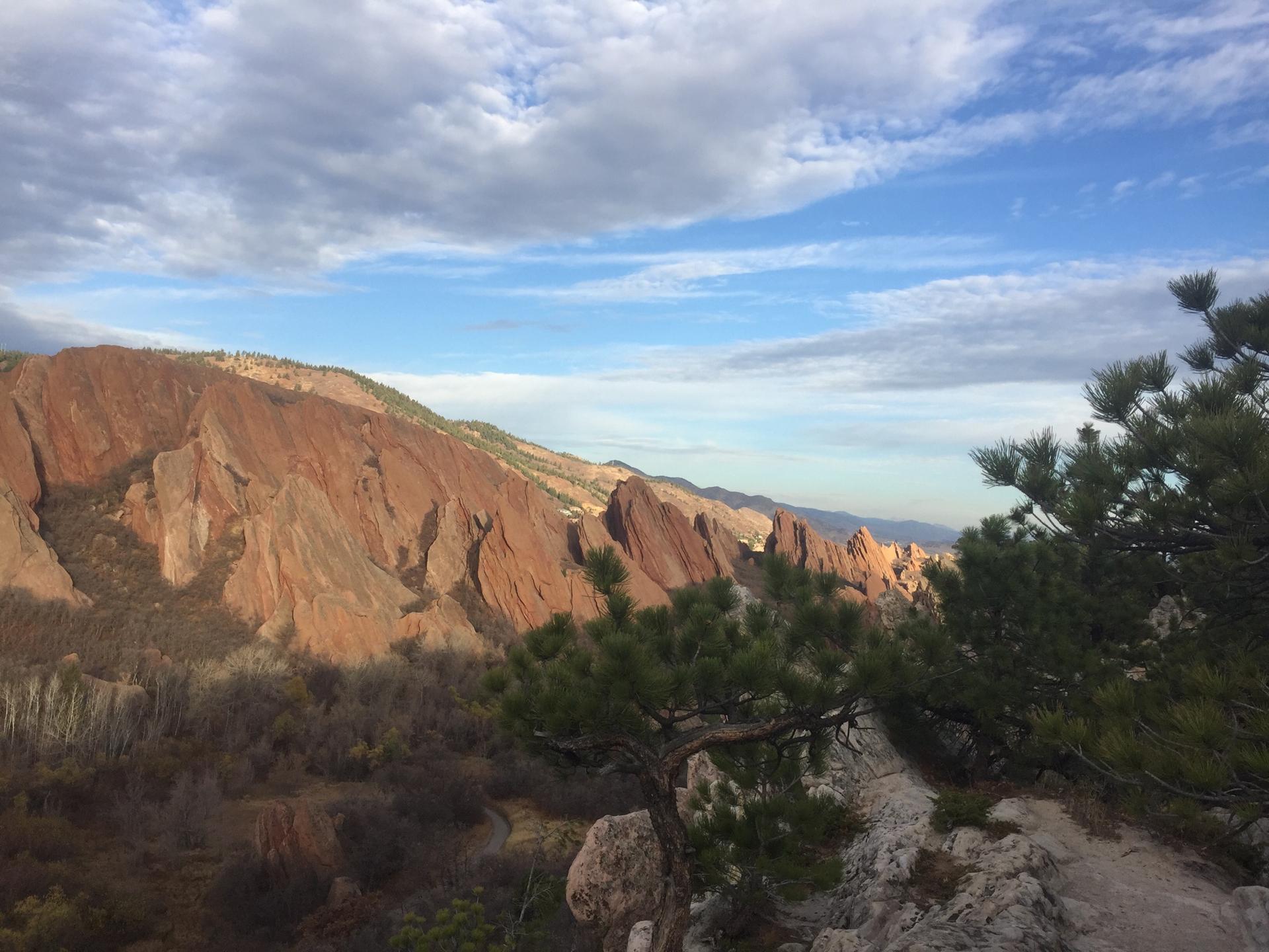 Panoramic view of red rock formations and green trees under a cloudy sky.