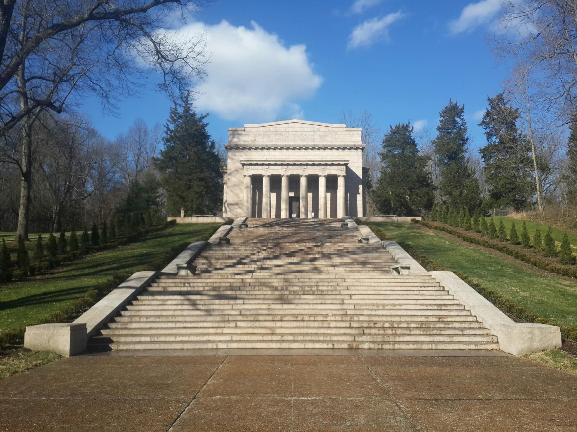 Classical stone building with columns atop wide stairs on a sunny day.