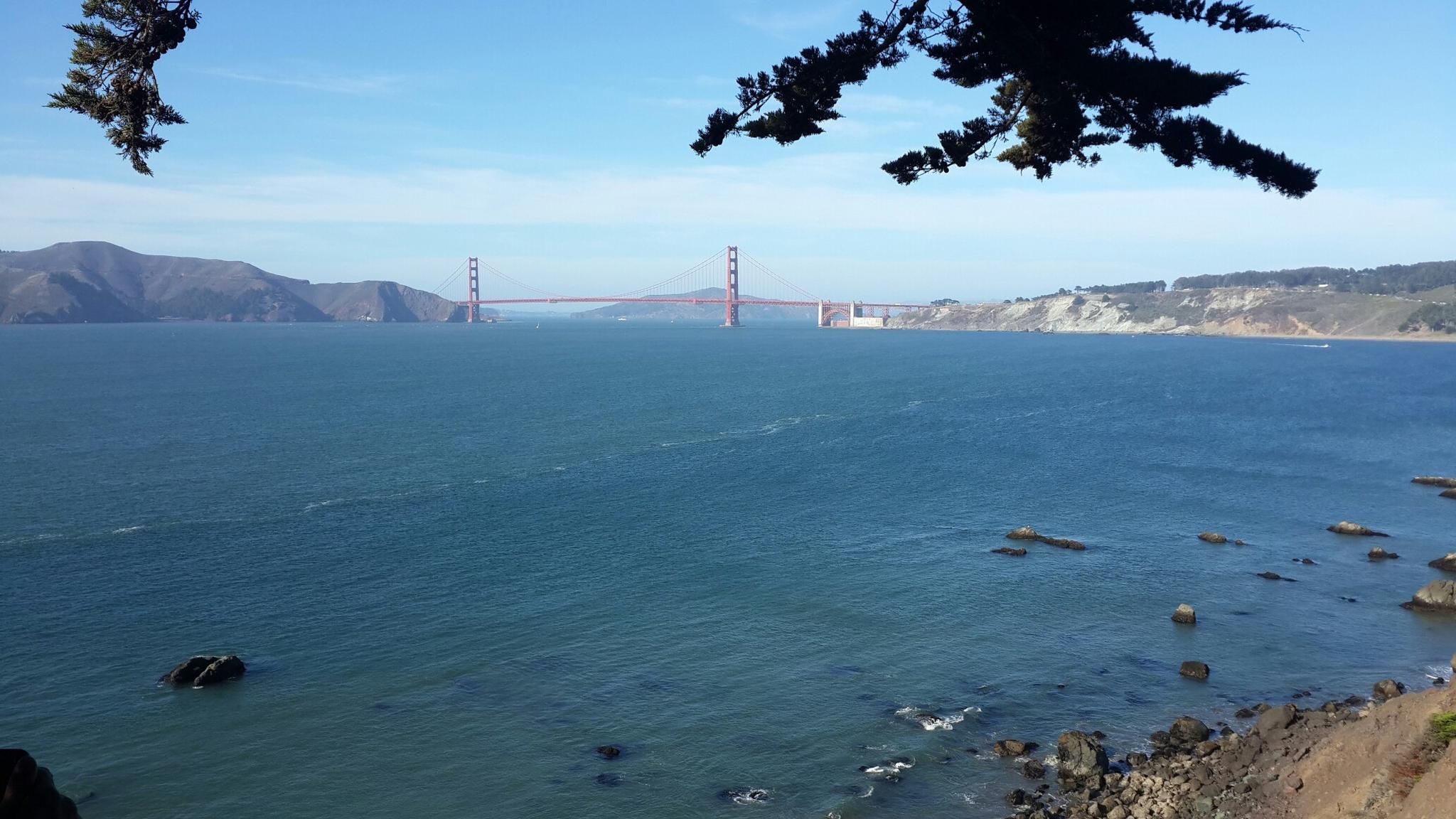 Expansive blue water with a distant red suspension bridge under a clear sky.
