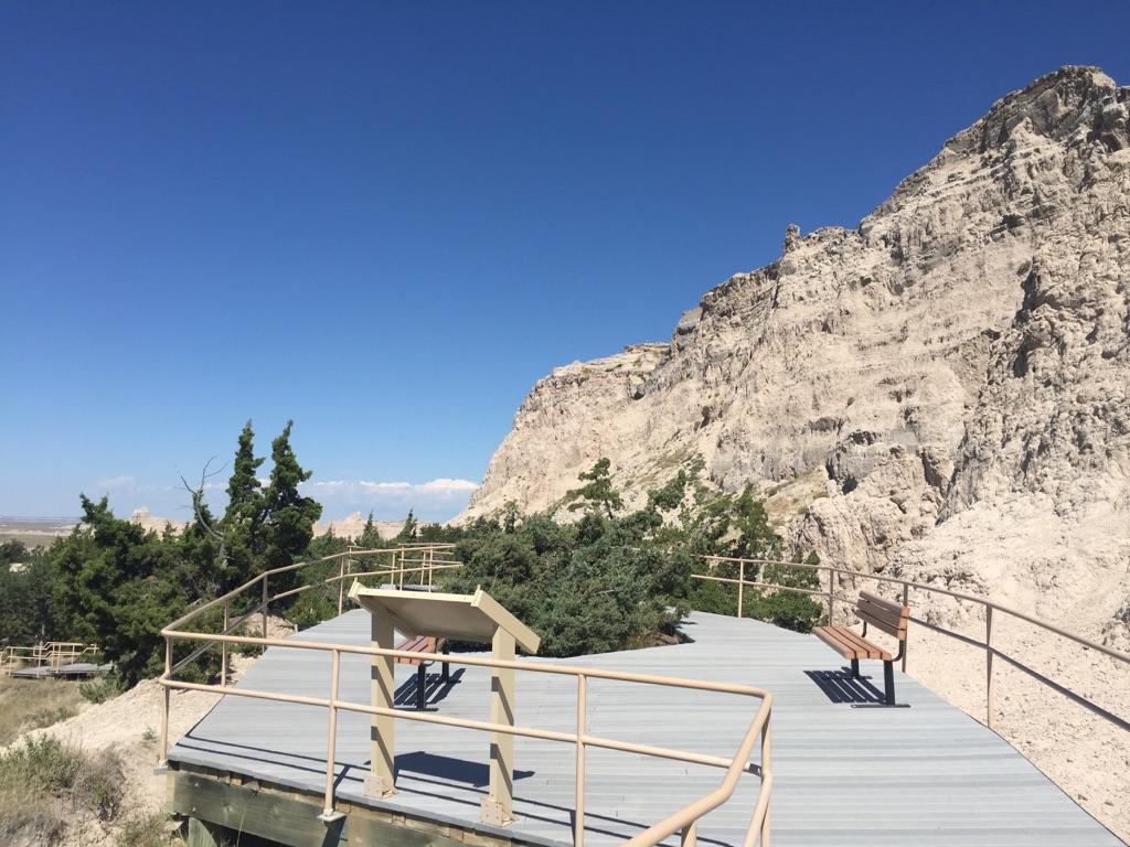 An observation deck with benches overlooks a vast, rocky landscape under a clear blue sky.