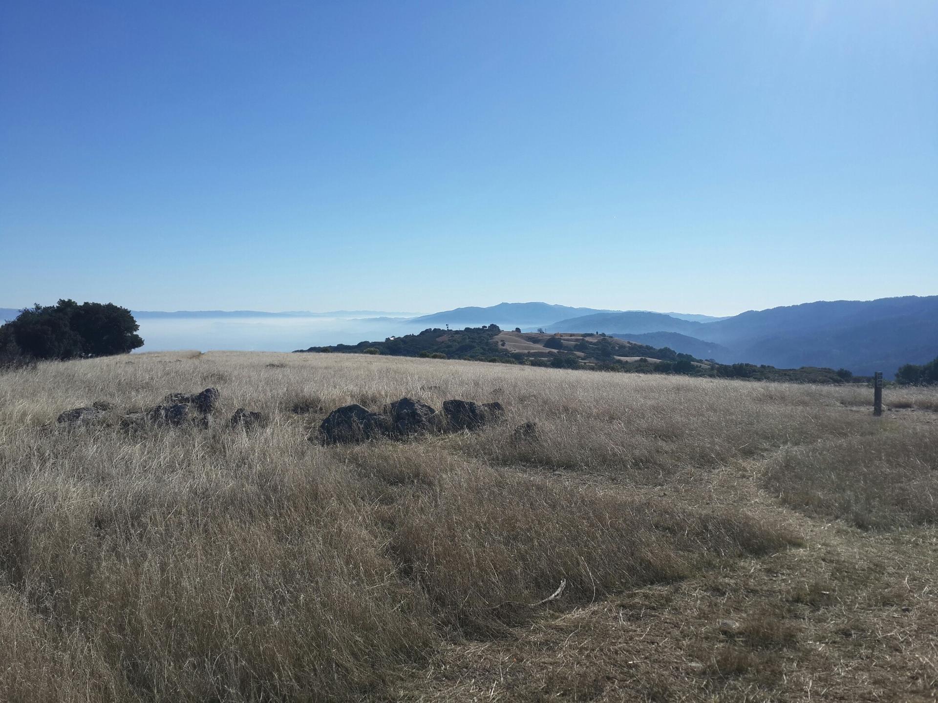 Expansive dry grass field on a hilltop overlooking foggy distant hills.