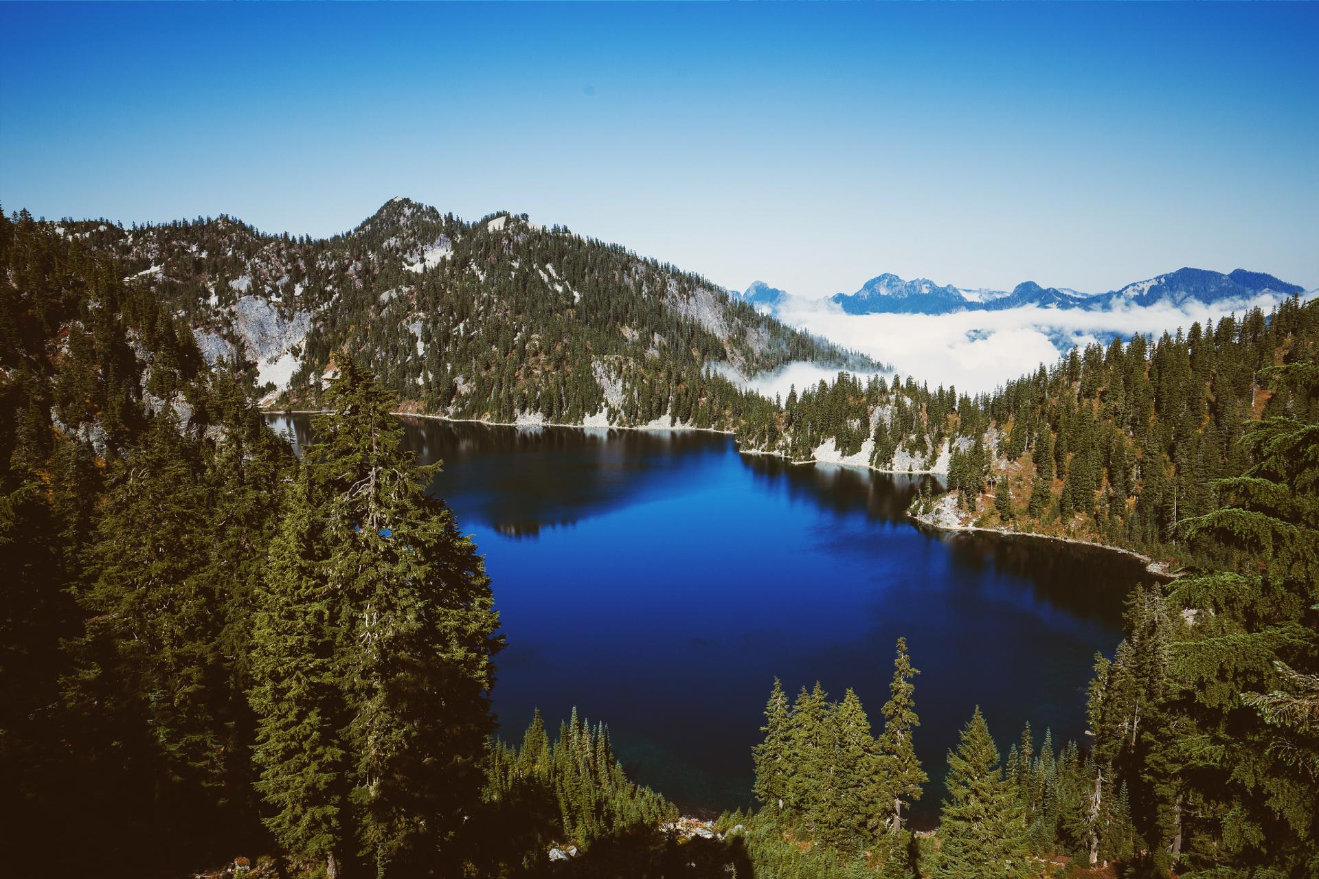 A deep blue lake surrounded by snow-dusted mountains and forests under a clear sky.
