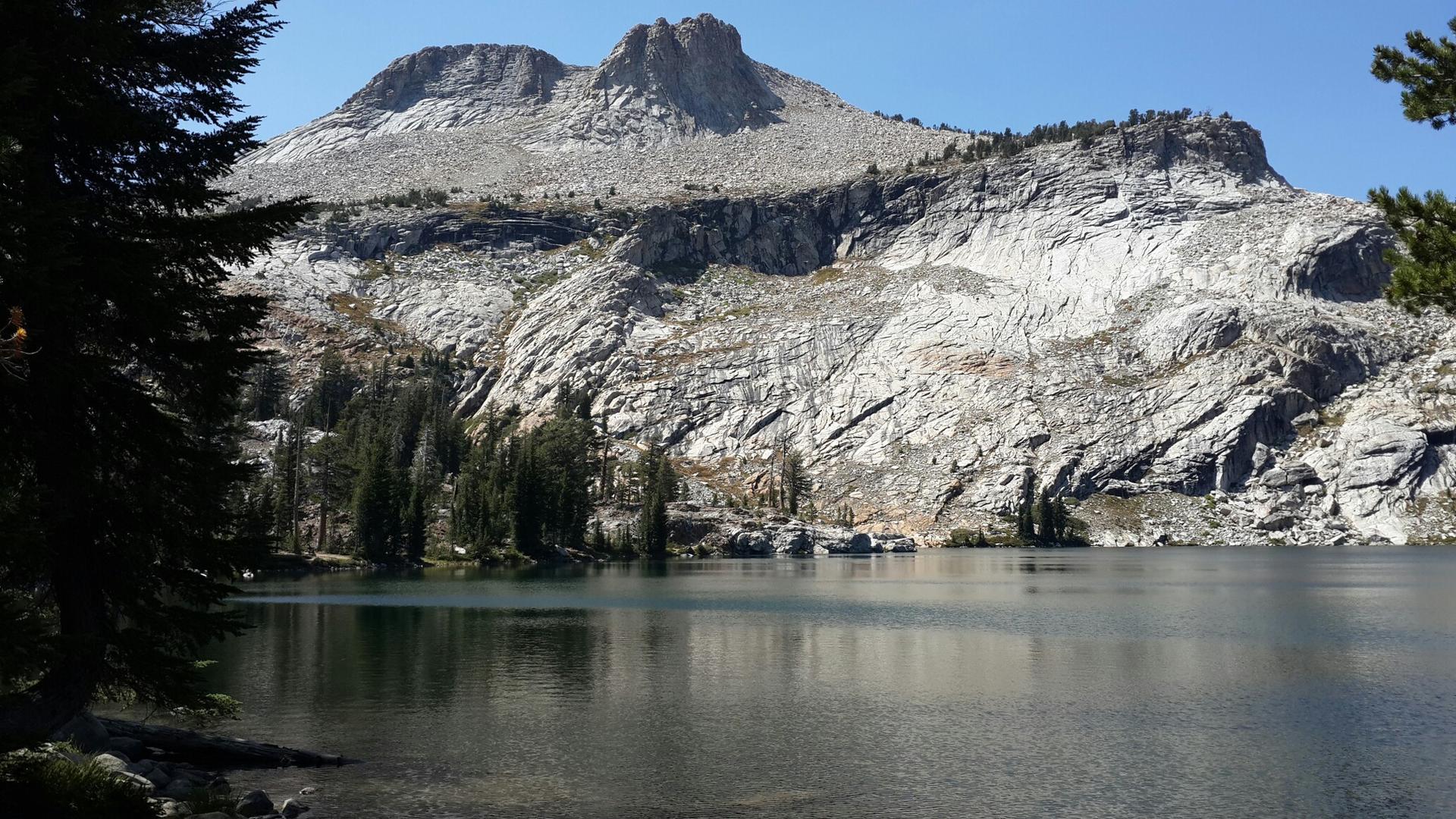Clear lake reflecting a massive, light-colored rocky mountain under bright sun.