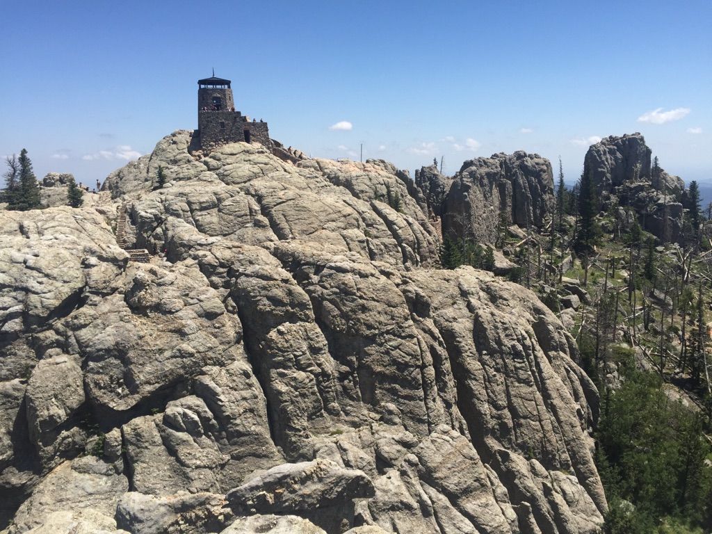 Stone lookout tower atop a rugged, rocky peak under a clear blue sky. - Black Elk Peak via Cathedral Spires Trail