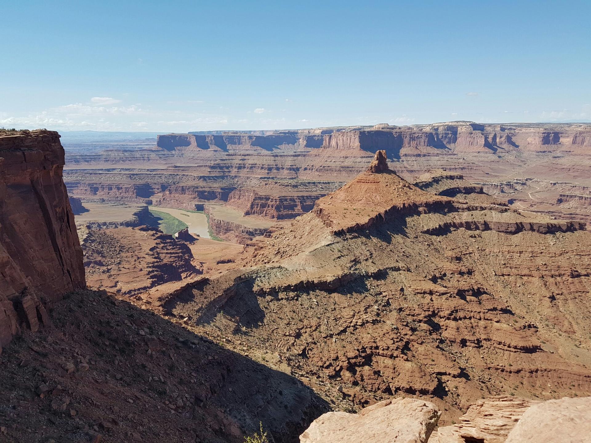 Sunny canyon vista with a prominent mesa and winding river below.