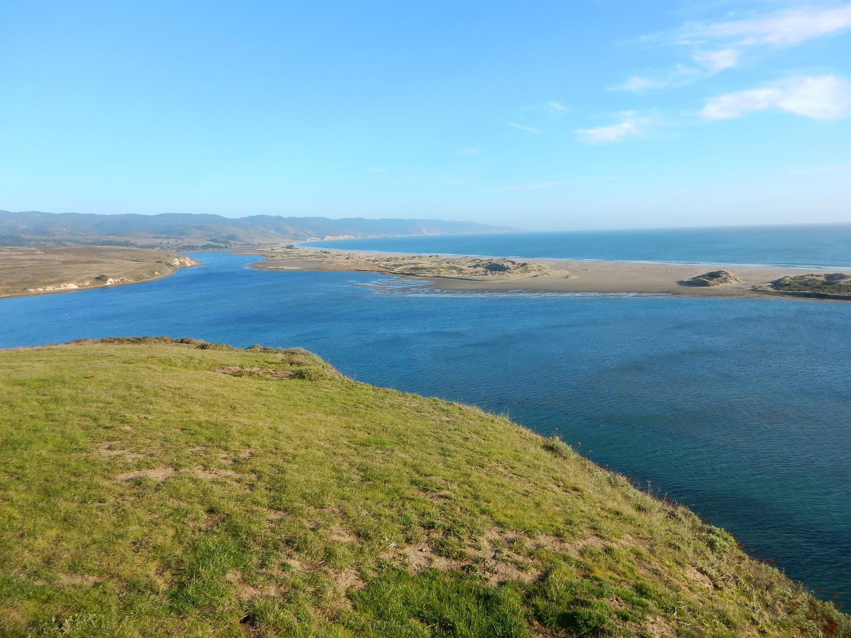 Expansive view of a blue estuary meeting the ocean under a bright sky.