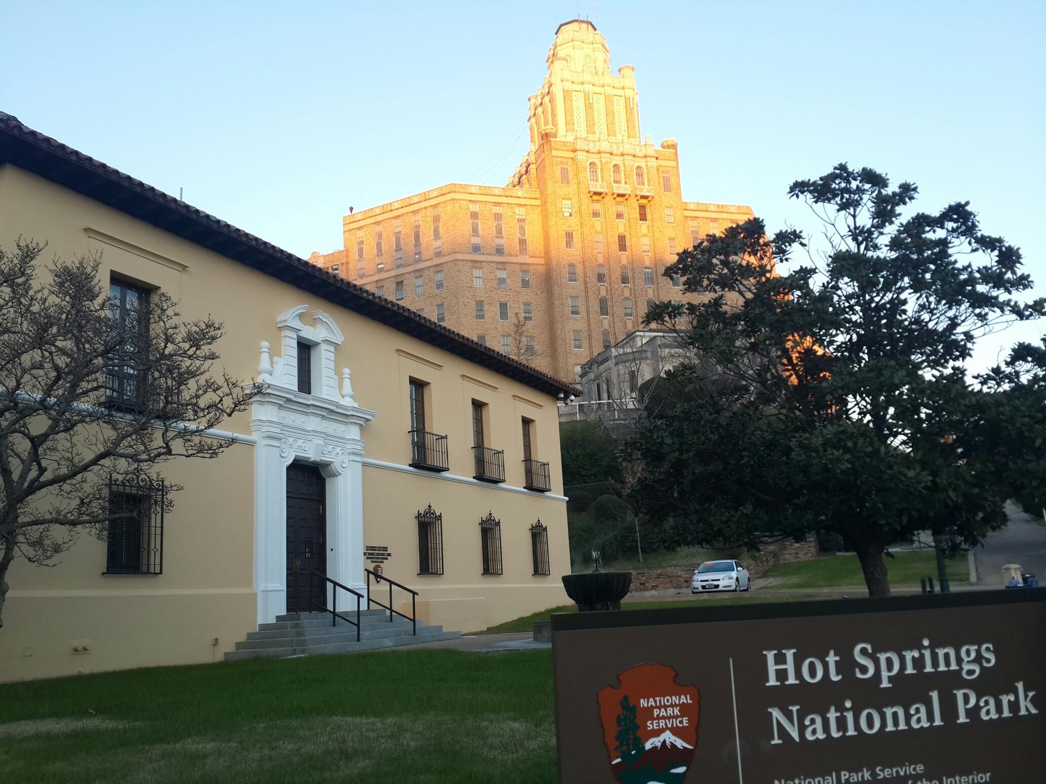 Golden light illuminates a grand building behind a smaller structure and sign.