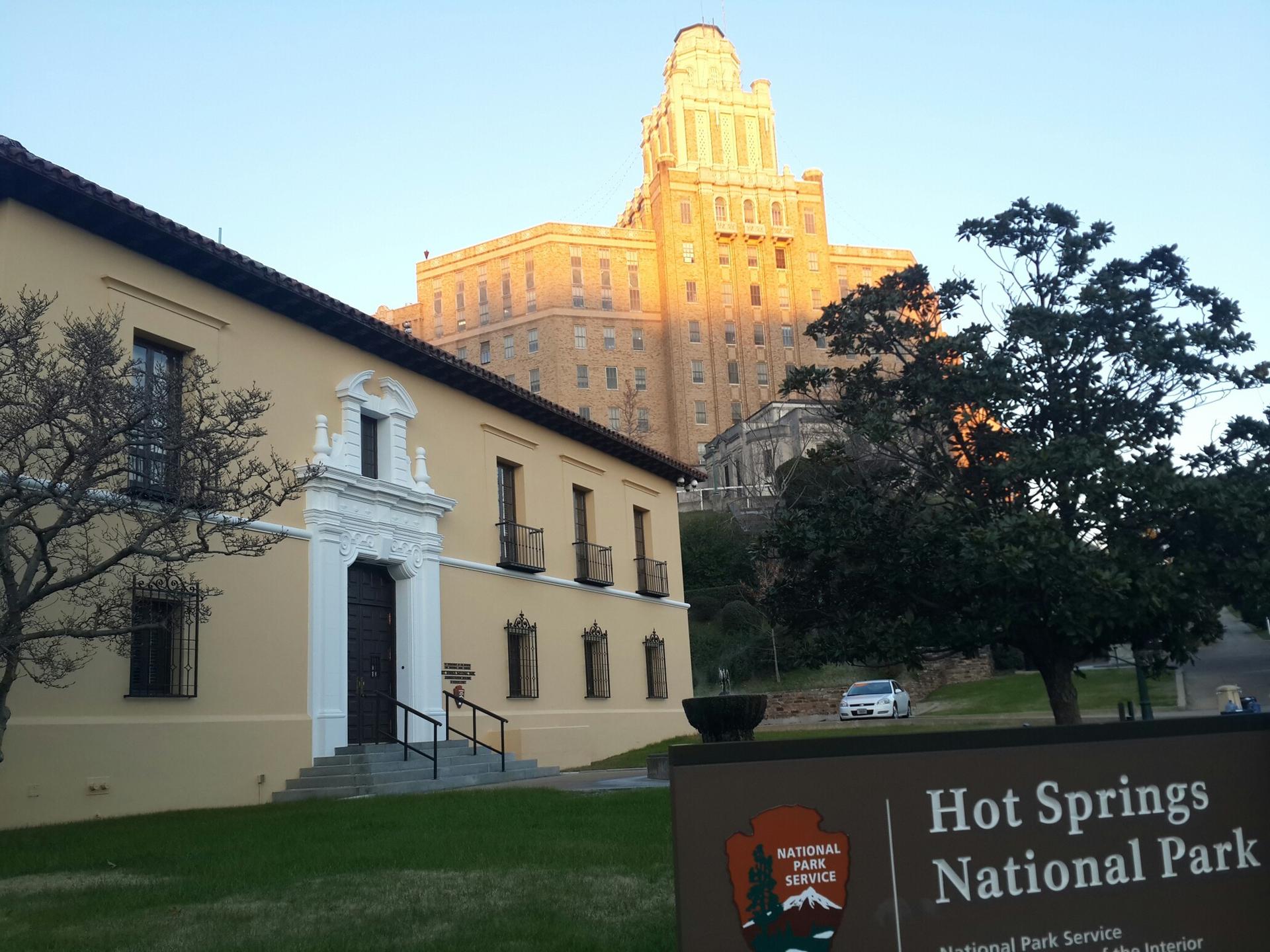 Golden light illuminates a grand building behind a smaller structure and sign.